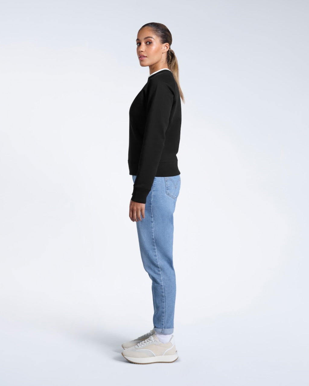 A full body photo of a woman side on looking back at the camera, modelling a black heavyweight organic cotton sweatshirt.