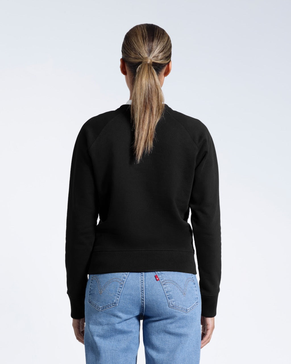 A woman facing away from the camera, showing the back of her black heavyweight organic cotton sweatshirt.