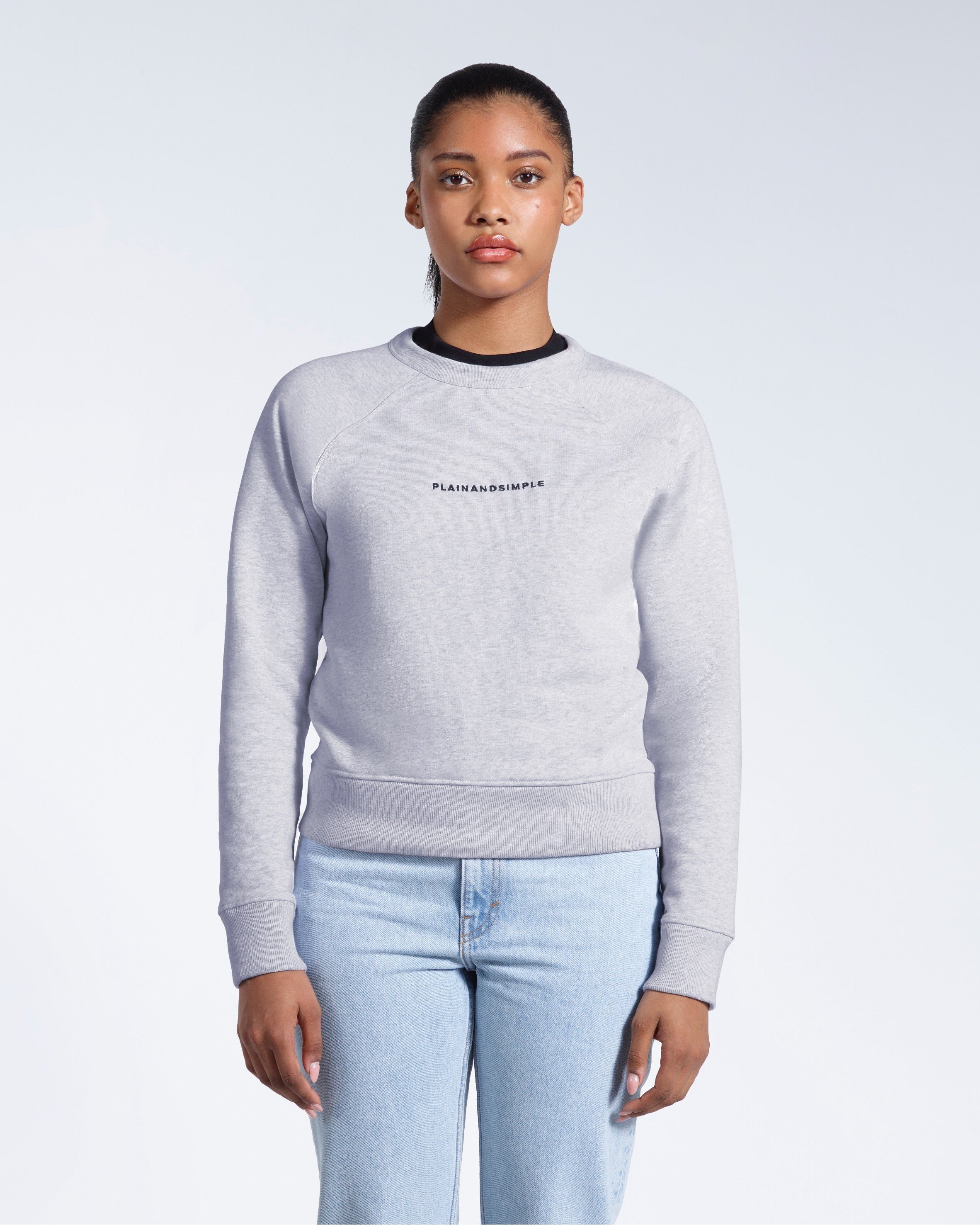 A woman face on with her arms by her side, modelling a branded grey heavyweight organic cotton sweatshirt.