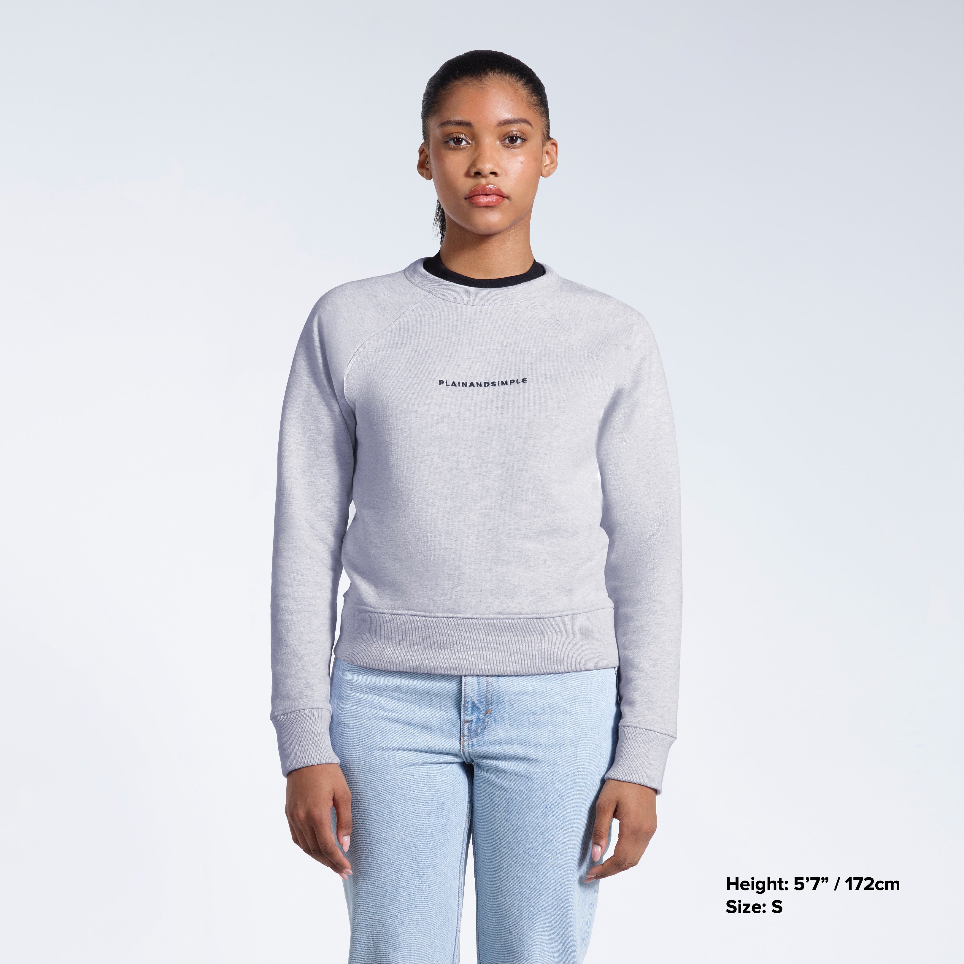 A woman face on with her arms by her side, modelling a branded grey heavyweight organic cotton sweatshirt.