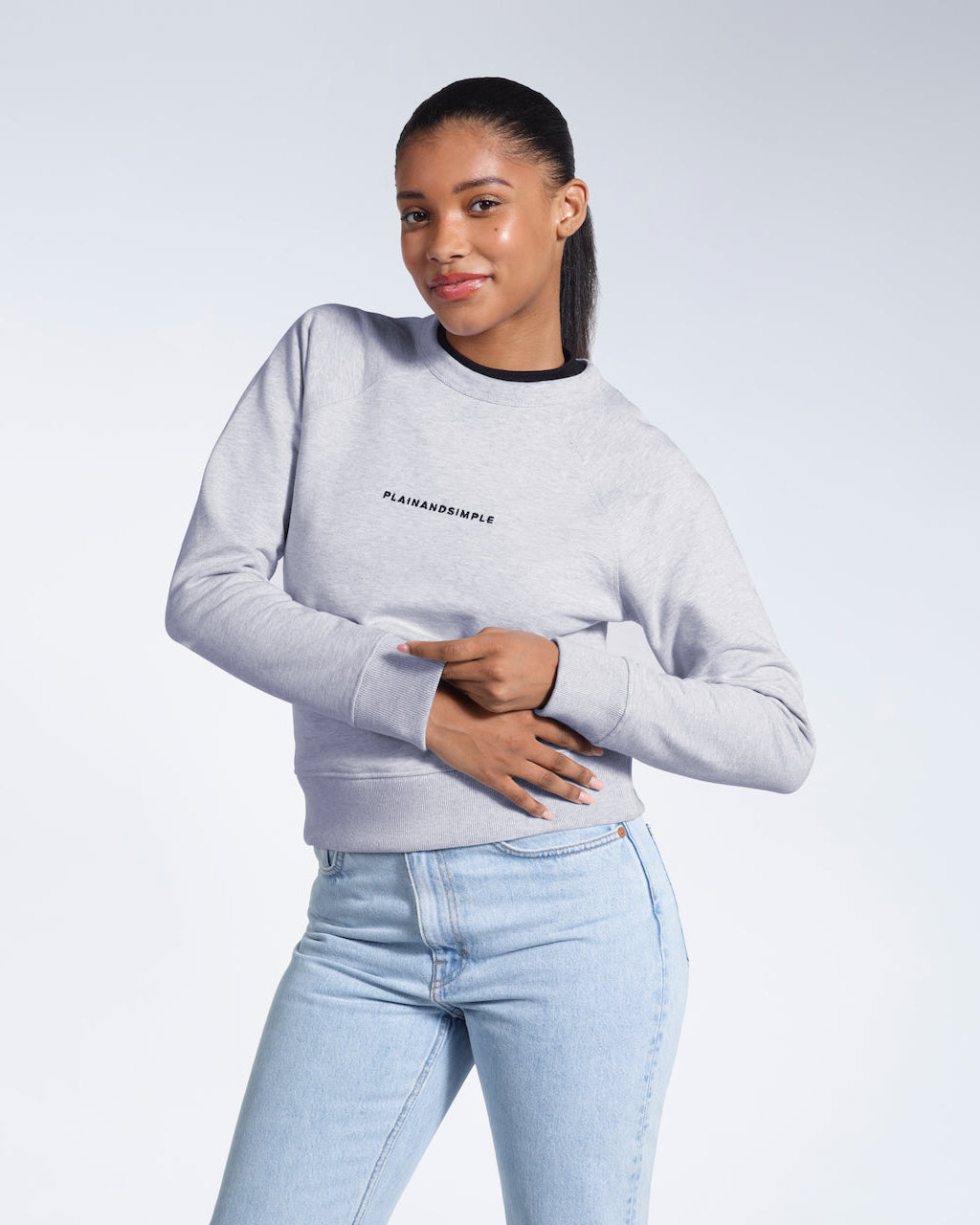 A woman smiling into the camera touching her hands, modelling a grey branded heavyweight organic cotton sweatshirt.