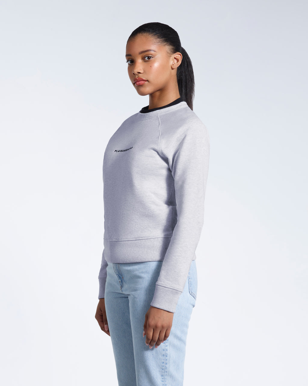A woman looking into the camera, modelling a grey branded heavyweight organic cotton sweatshirt.