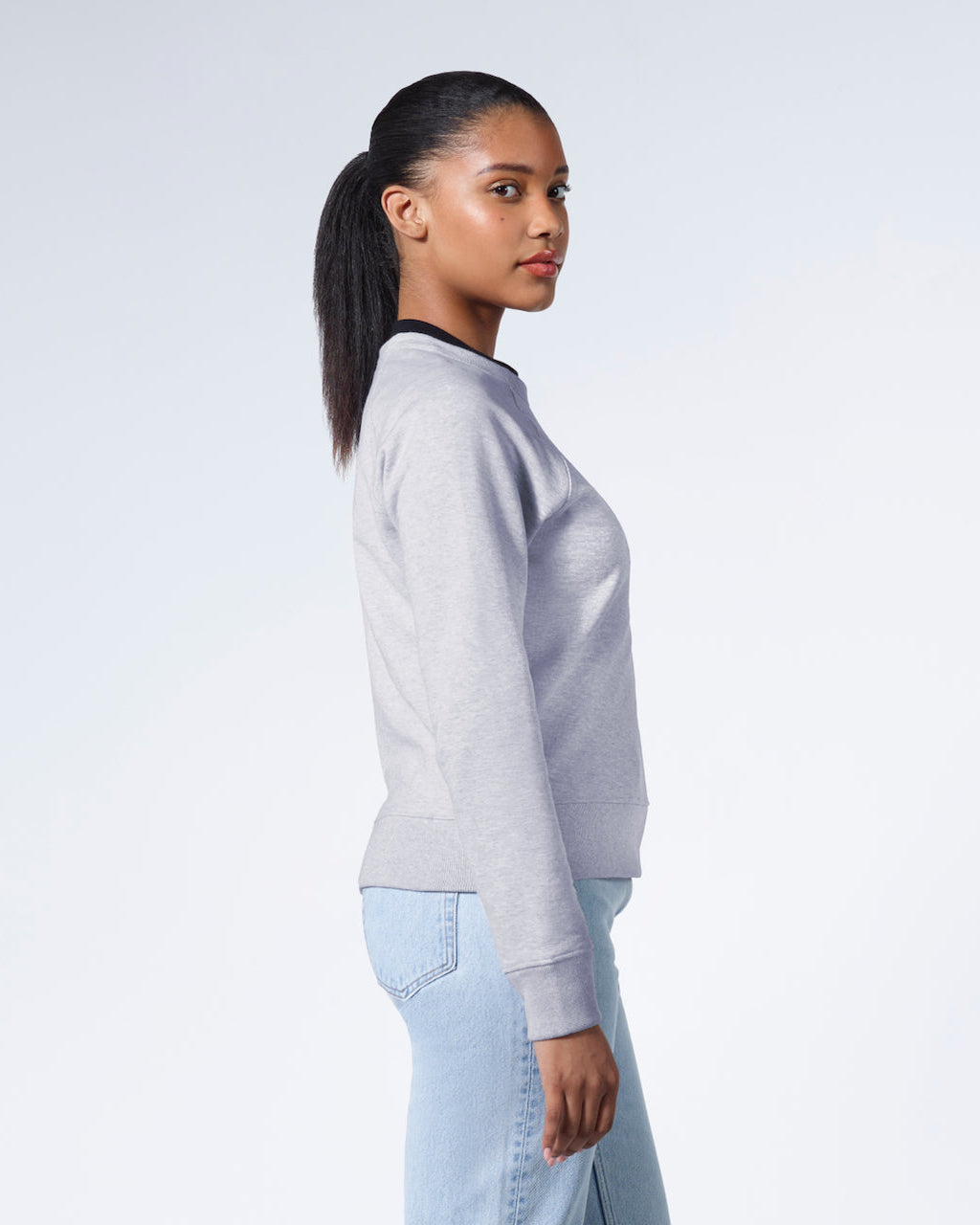 A woman side on looking back at the camera, modelling a grey heavyweight organic cotton sweatshirt.