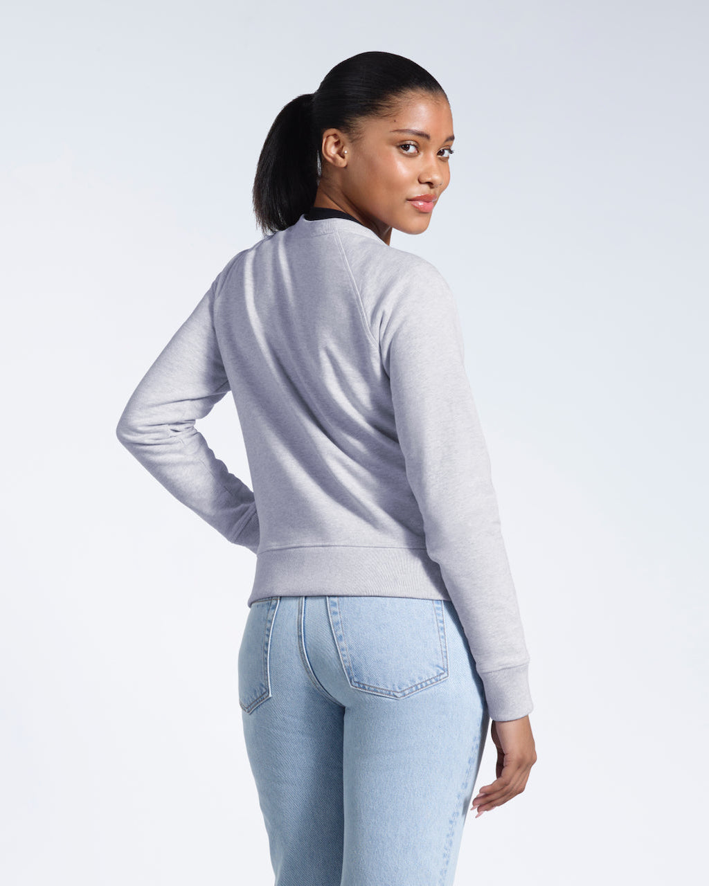 A woman looking back at the camera, showing the back of her grey heavyweight organic cotton sweatshirt.
