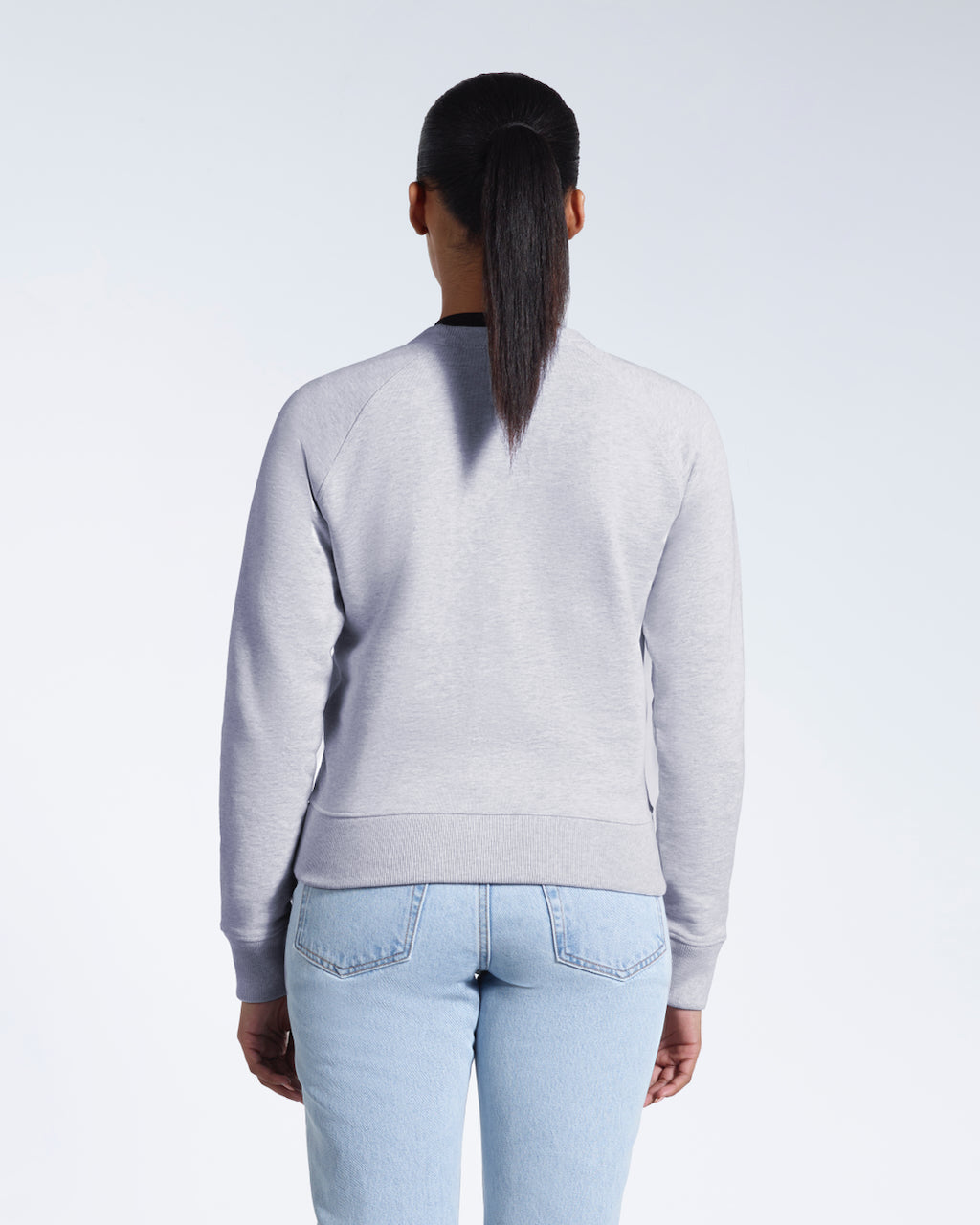 A woman facing away from the camera, showing the back of her grey heavyweight organic cotton sweatshirt.