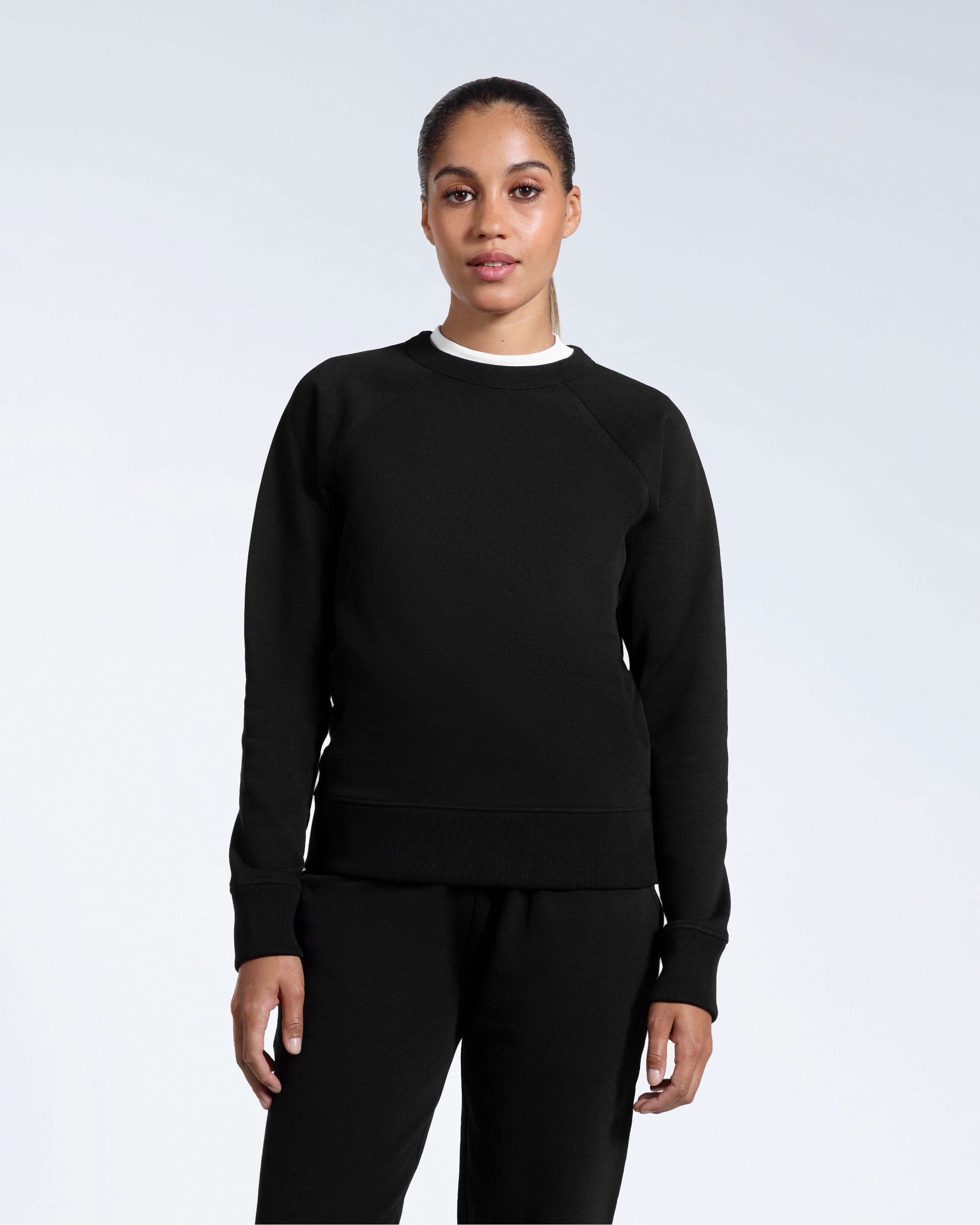 A woman face on with her arms by her side, modelling a black heavyweight organic cotton sweatshirt with matching joggers.