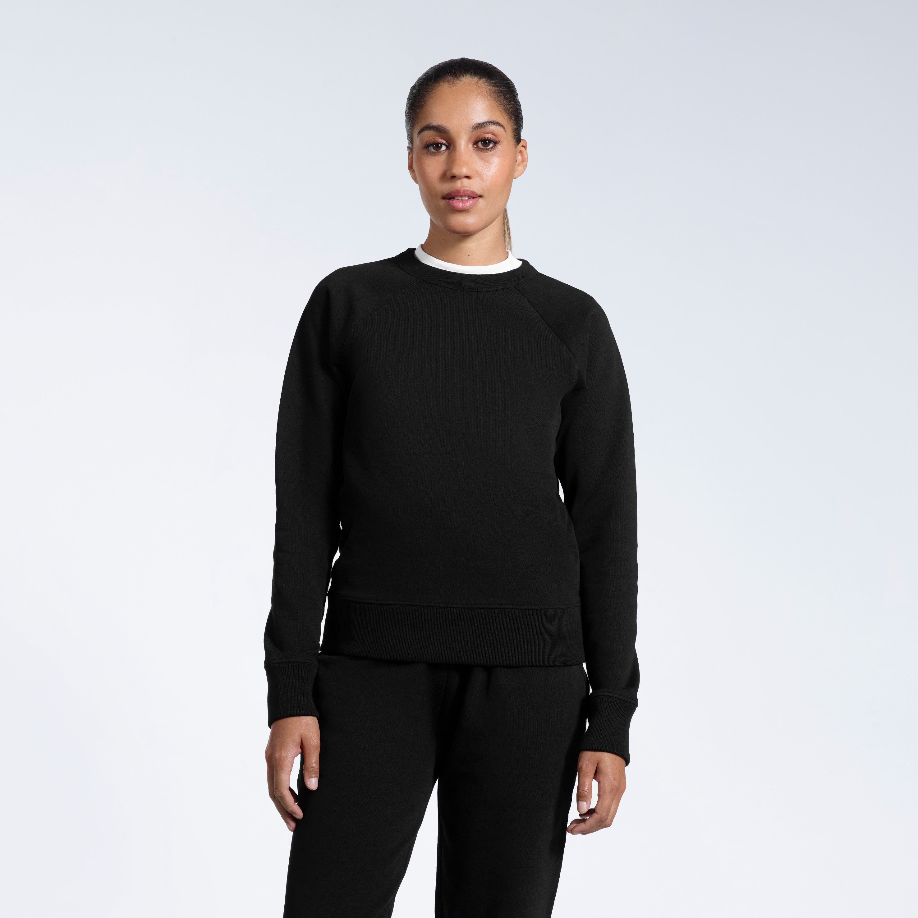 A woman face on with her arms by her side, modelling a black heavyweight organic cotton sweatshirt with matching joggers.