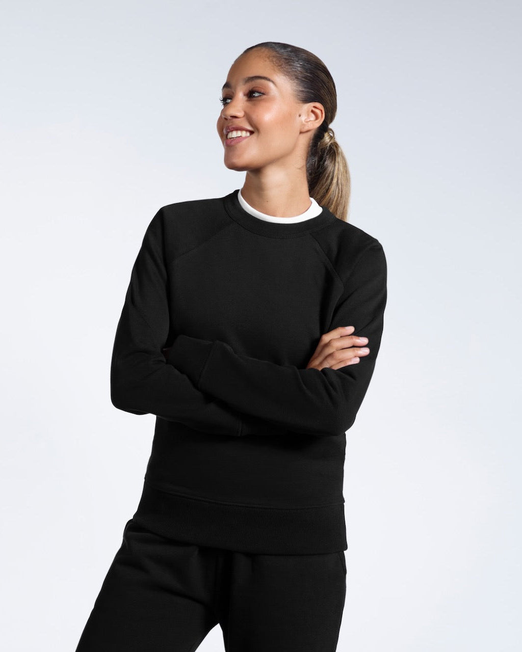 A woman smiling with her arms folded, modelling a black heavyweight organic cotton sweatshirt with matching joggers.