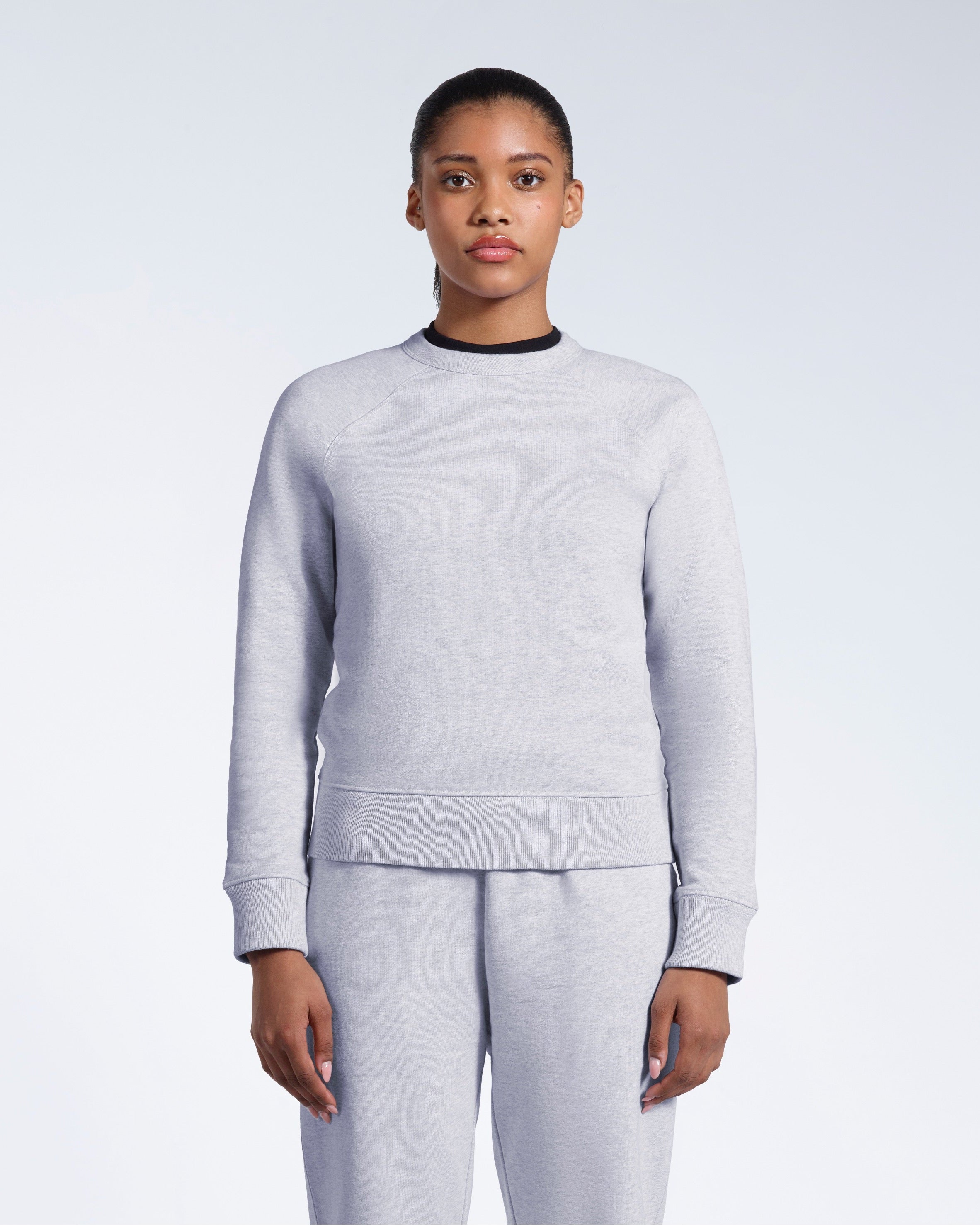 A woman face on with her arms by her side, modelling a grey heavyweight organic cotton sweatshirt with matching joggers.