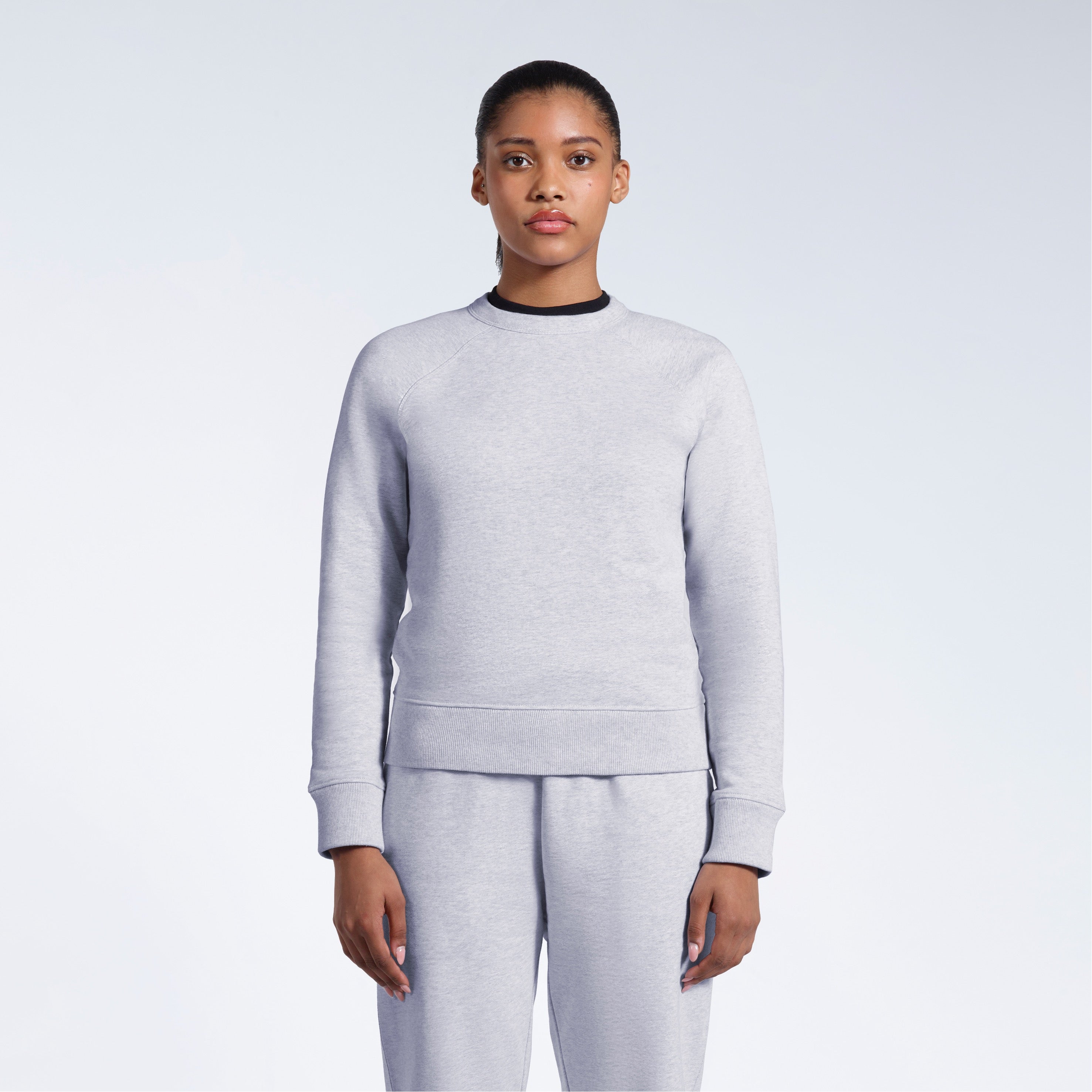 A woman face on with her arms by her side, modelling a grey heavyweight organic cotton sweatshirt with matching joggers.