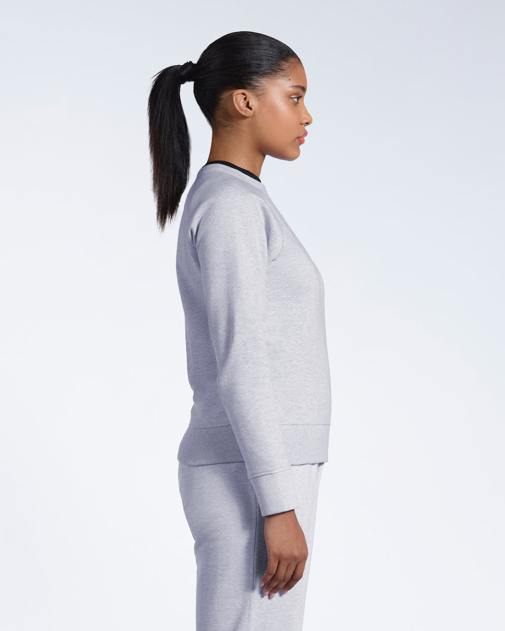 A woman facing side on, modelling a grey heavyweight organic cotton sweatshirt with matching joggers.