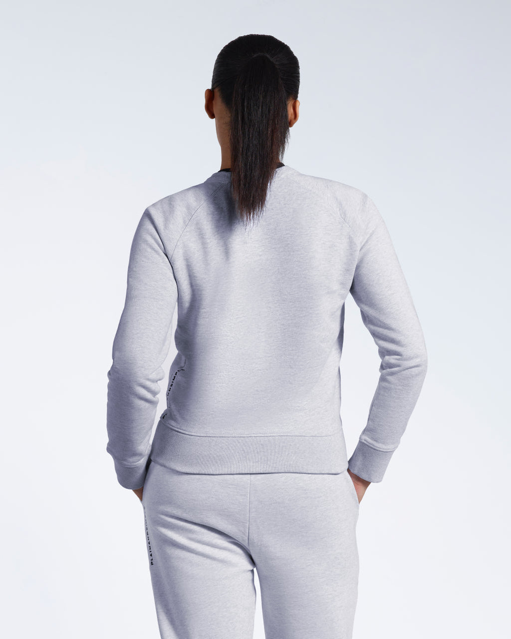 A woman facing away from the camera, showing the back of her grey heavyweight organic cotton sweatshirt with matching joggers.