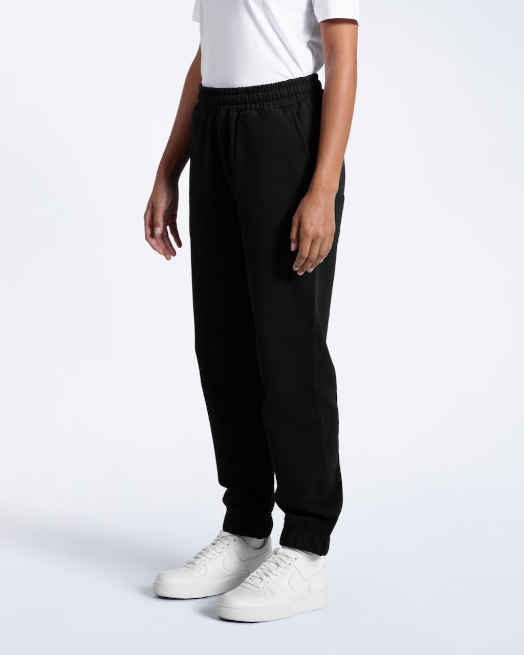 A person facing side on, modelling a pair of women's black heavyweight organic cotton joggers.