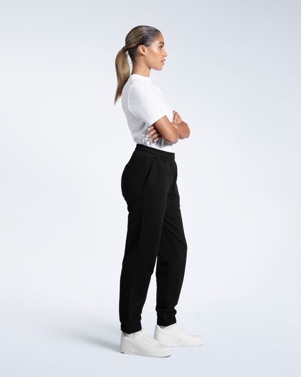 A woman facibg side on with her arms folded, modelling a pair of black heavyweight organic cotton joggers.