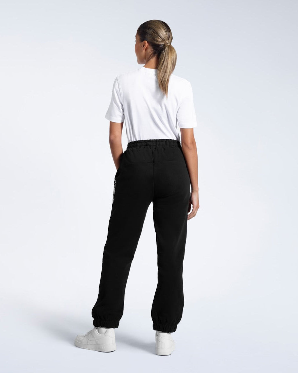 A woman with her back to the camera with her arms by her sides, modelling a pair of black heavyweight organic cotton joggers.