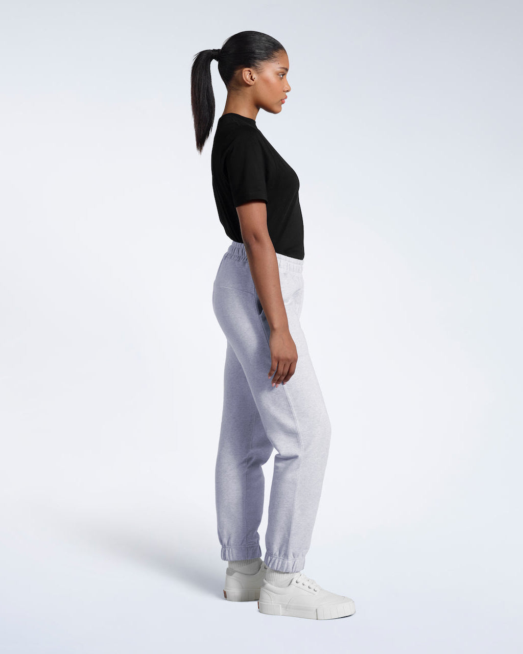 A woman facing side on with her arms by her sides, modelling a pair of grey heavyweight organic cotton joggers.