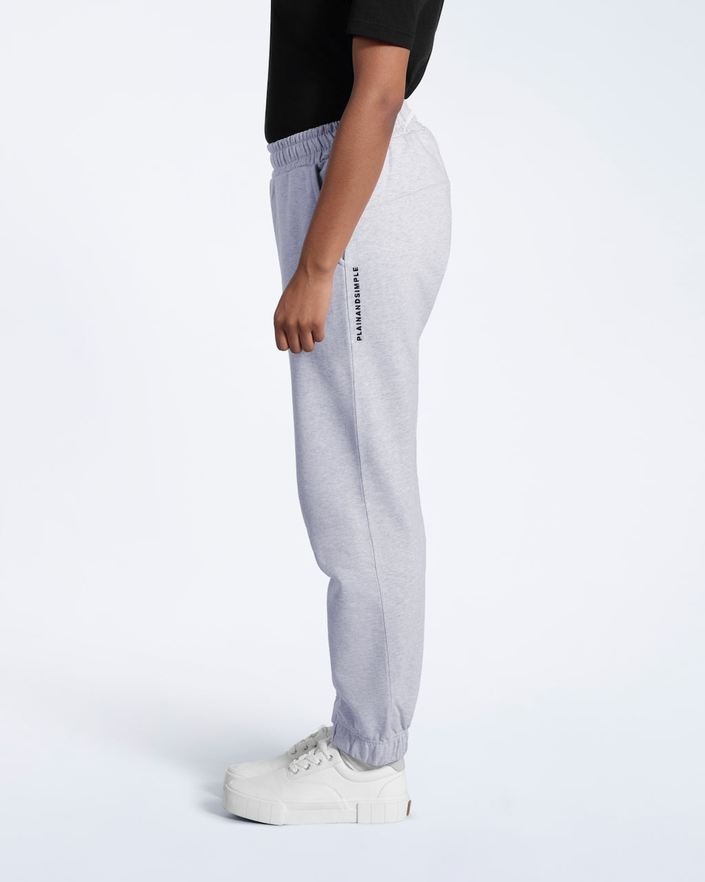 A person facing side on, modelling a pair of women's grey heavyweight organic cotton joggers.