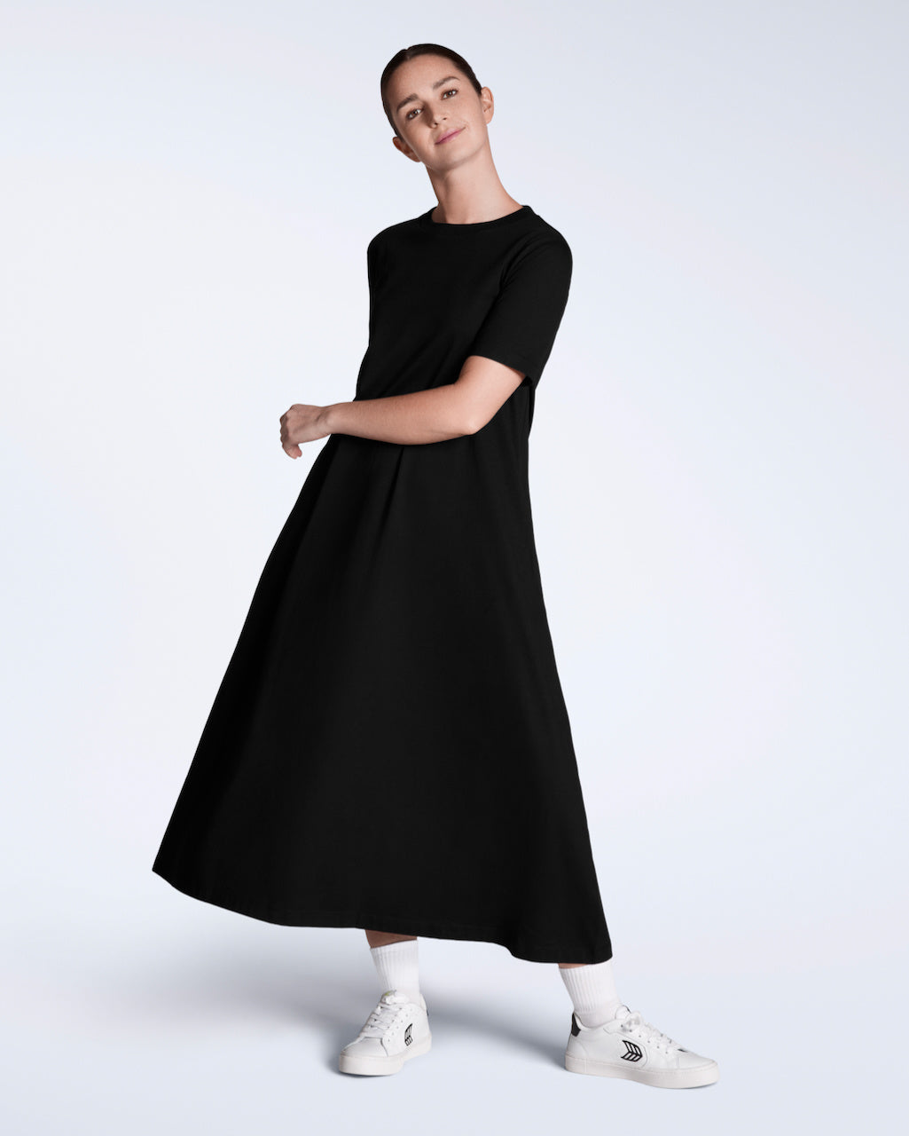 A woman smiling into the camera, modelling a plain black, long line, maxi organic cotton t shirt dress.