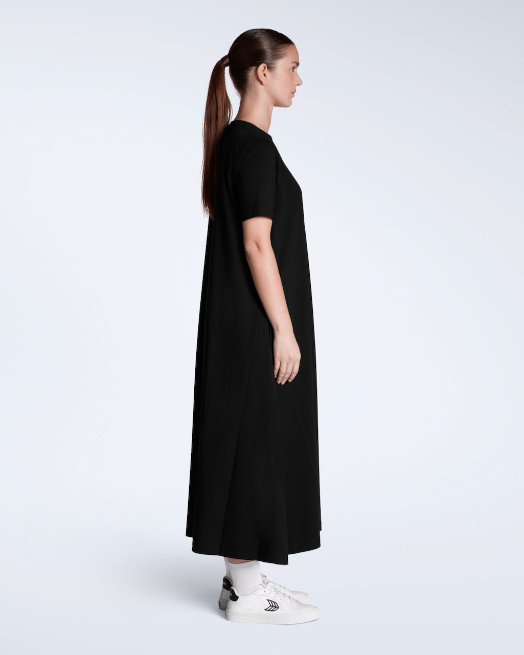A woman facing side on with her arms by her side, modelling a plain black, long line, maxi organic cotton t shirt dress.