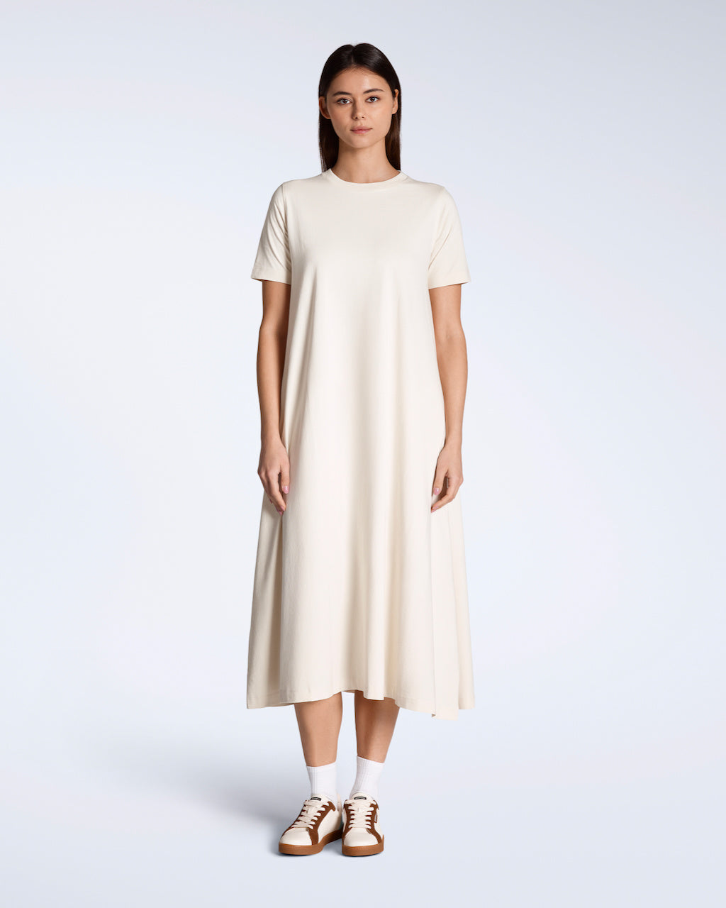 A woman facing front on with her arms by her side, modelling a plain natural coloured, long line, maxi organic cotton t shirt dress.