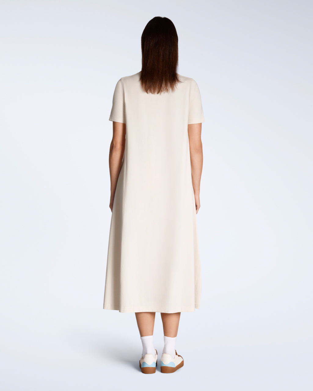 A woman facing away from the camera, modelling a plain natural coloured, long line, maxi organic cotton t shirt dress.