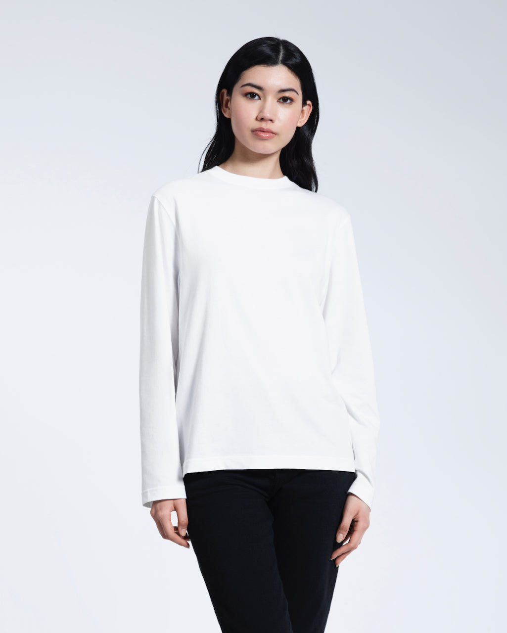 A woman standing front on with her arms by her sides, modelling a plain white long sleeve organic cotton t shirt.