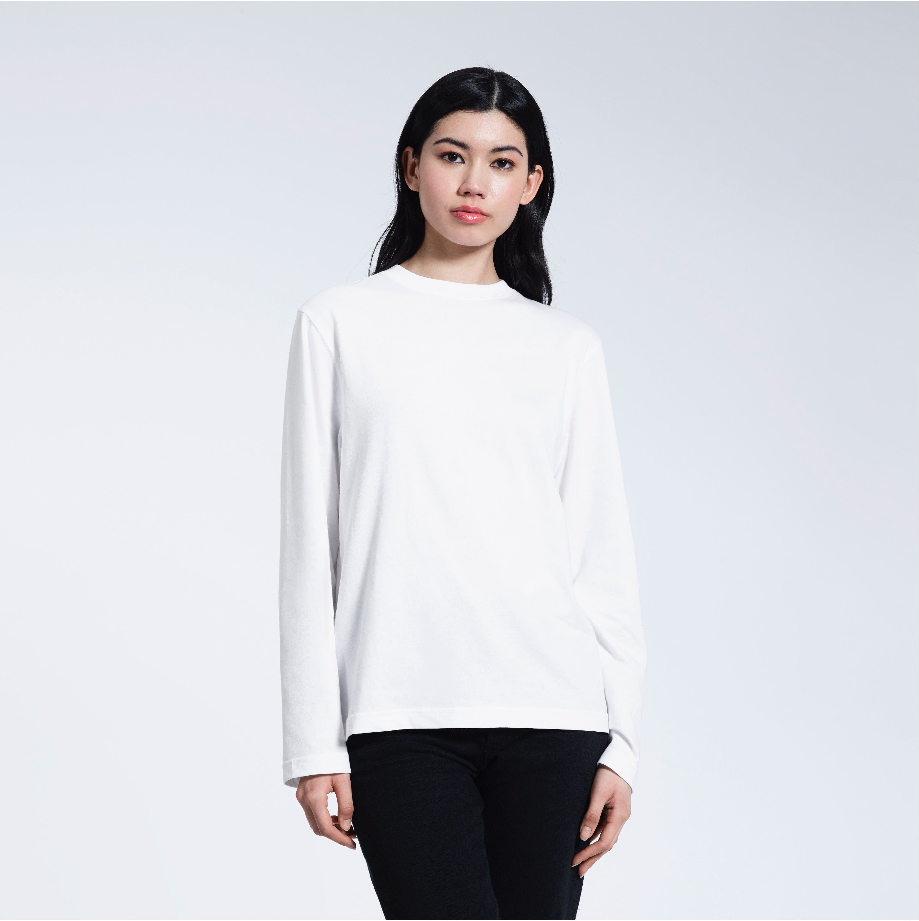 A woman standing front on with her arms by her sides, modelling a plain white long sleeve organic cotton t shirt.