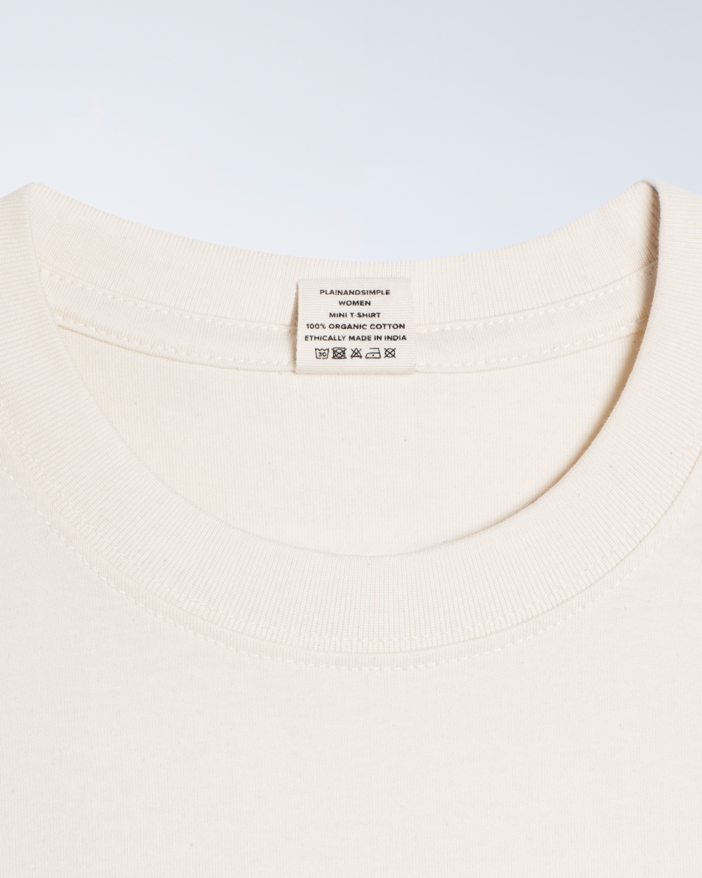 A close up of a neck label, for a natural coloured, organic cotton mini t shirt.