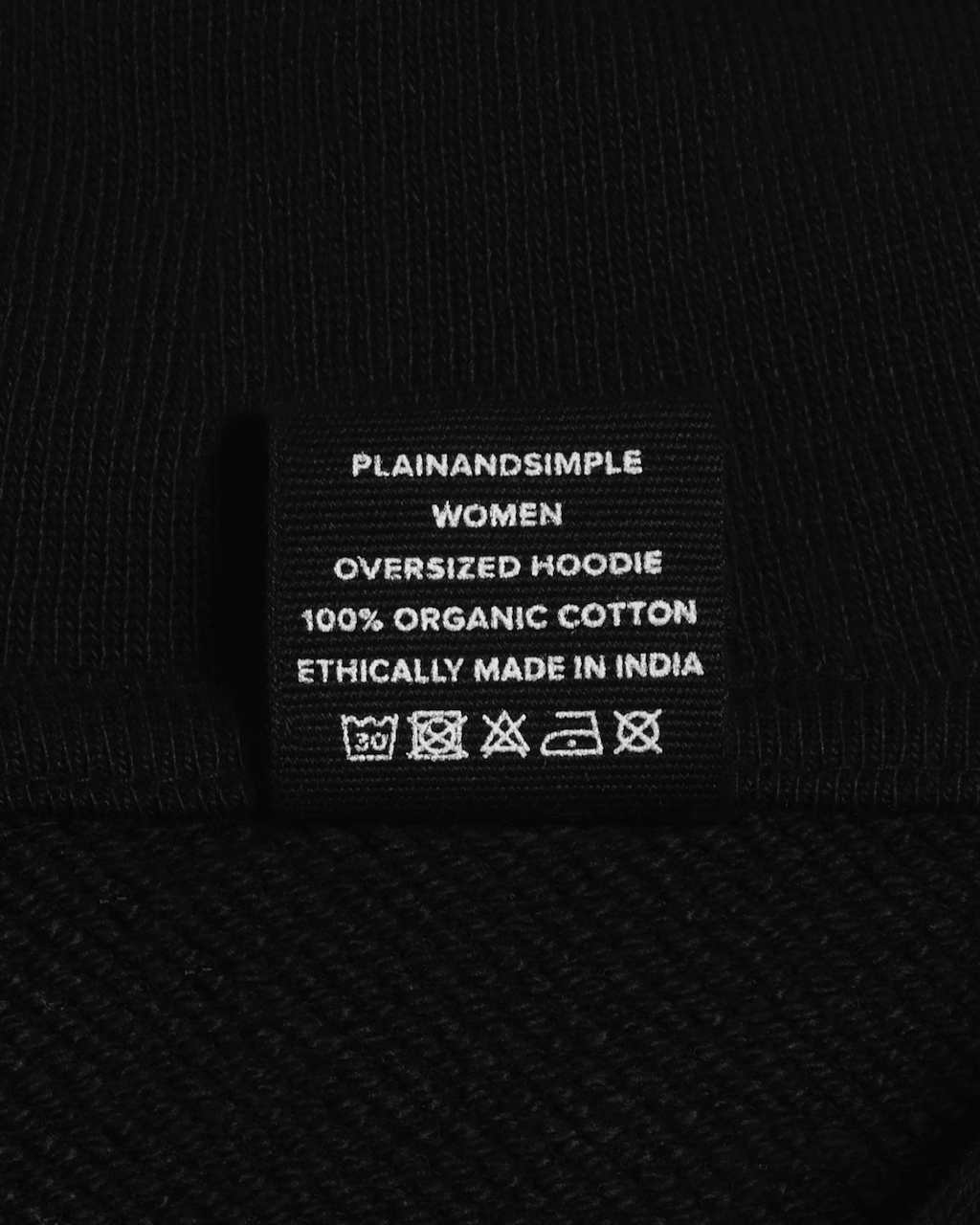 A close up of the neck label in a black, oversized, organic cotton hoodie.
