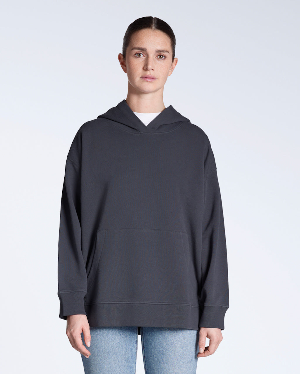 A woman facing front on, modelling a plain dark grey, oversized, organic cotton hoodie.