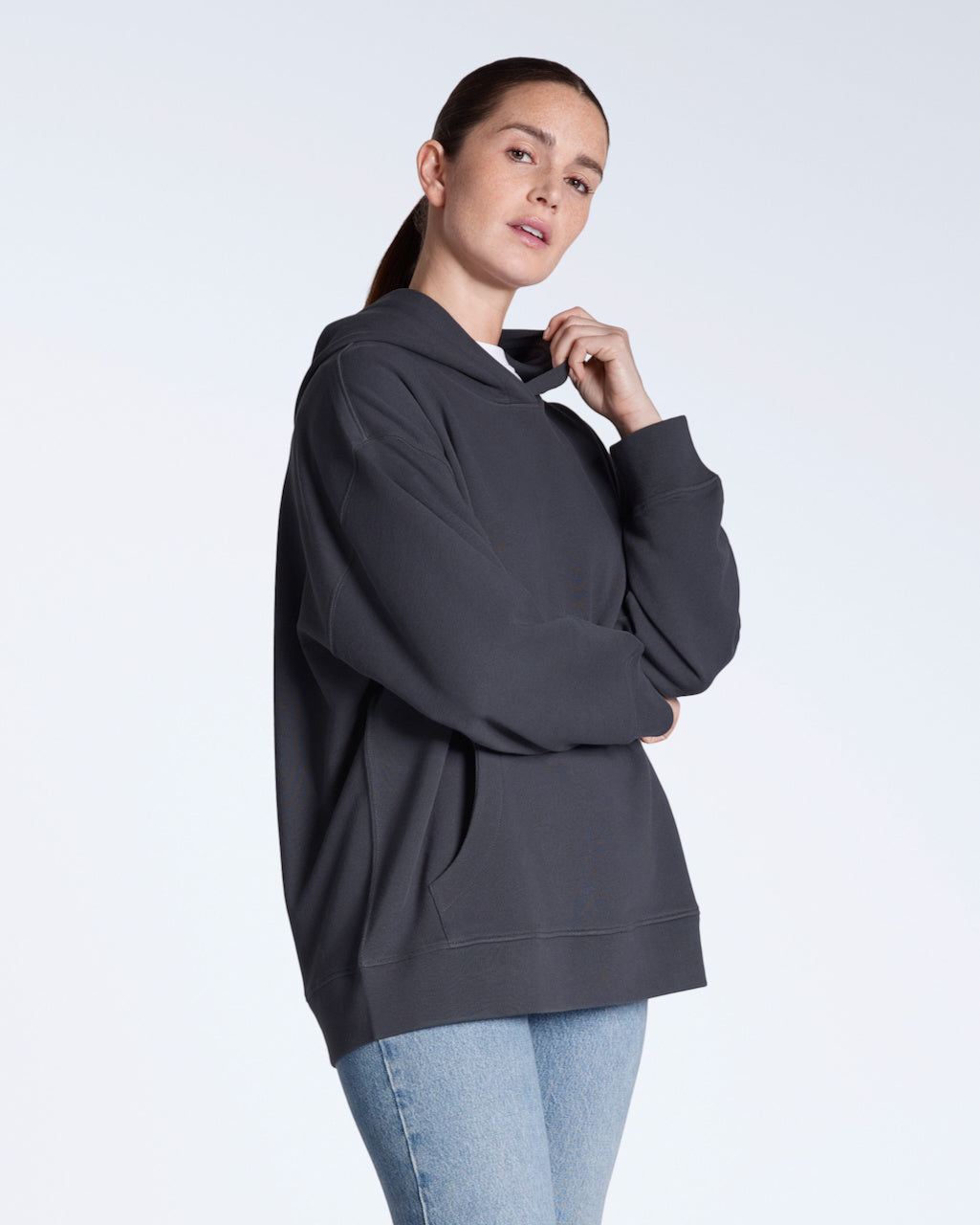 A woman looking into the camera with her arms crossed, modelling a plain dark grey, oversized, organic cotton hoodie.