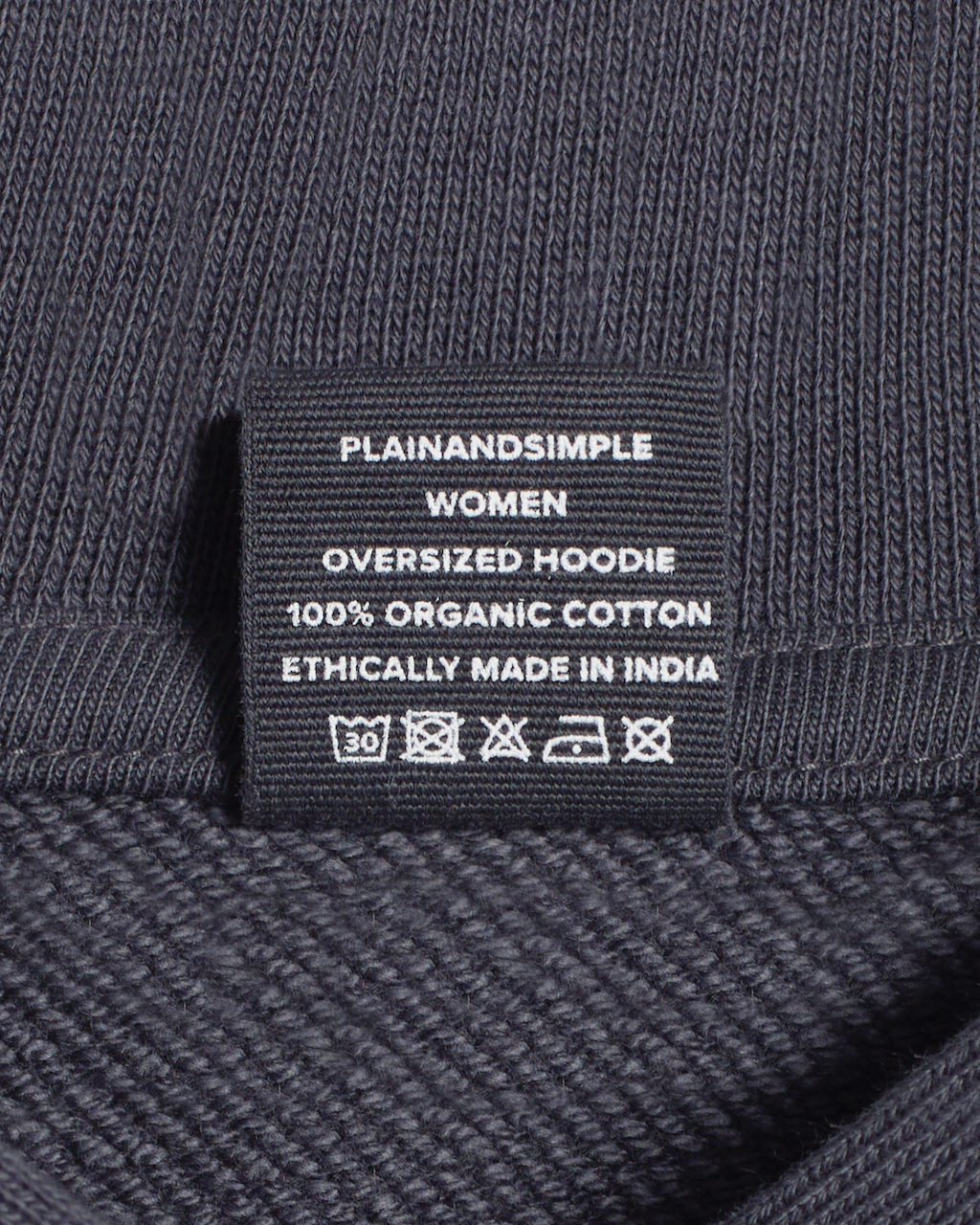 A close up of the neck label in a dark grey, oversized, organic cotton hoodie.