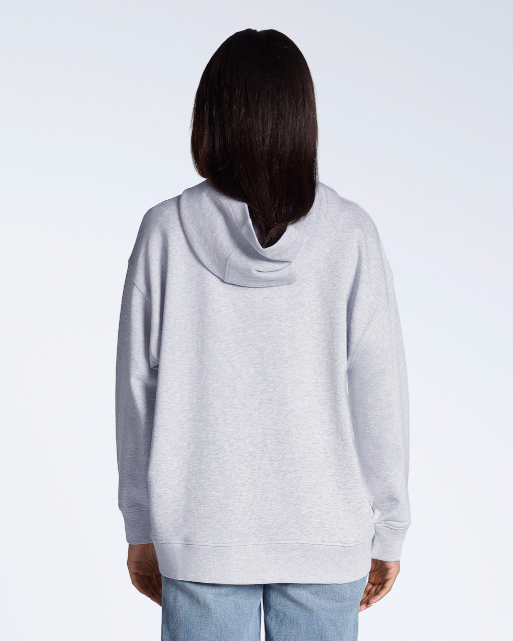 A woman facing away from the camera with her hands by her sides, modelling a plain grey, oversized, organic cotton hoodie.