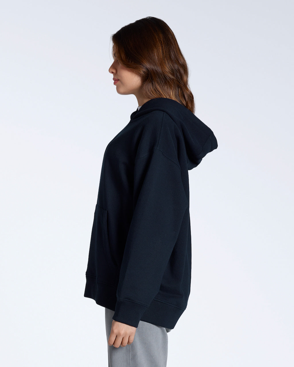 A woman facing side on, modelling a plain nayy, oversized, organic cotton hoodie.