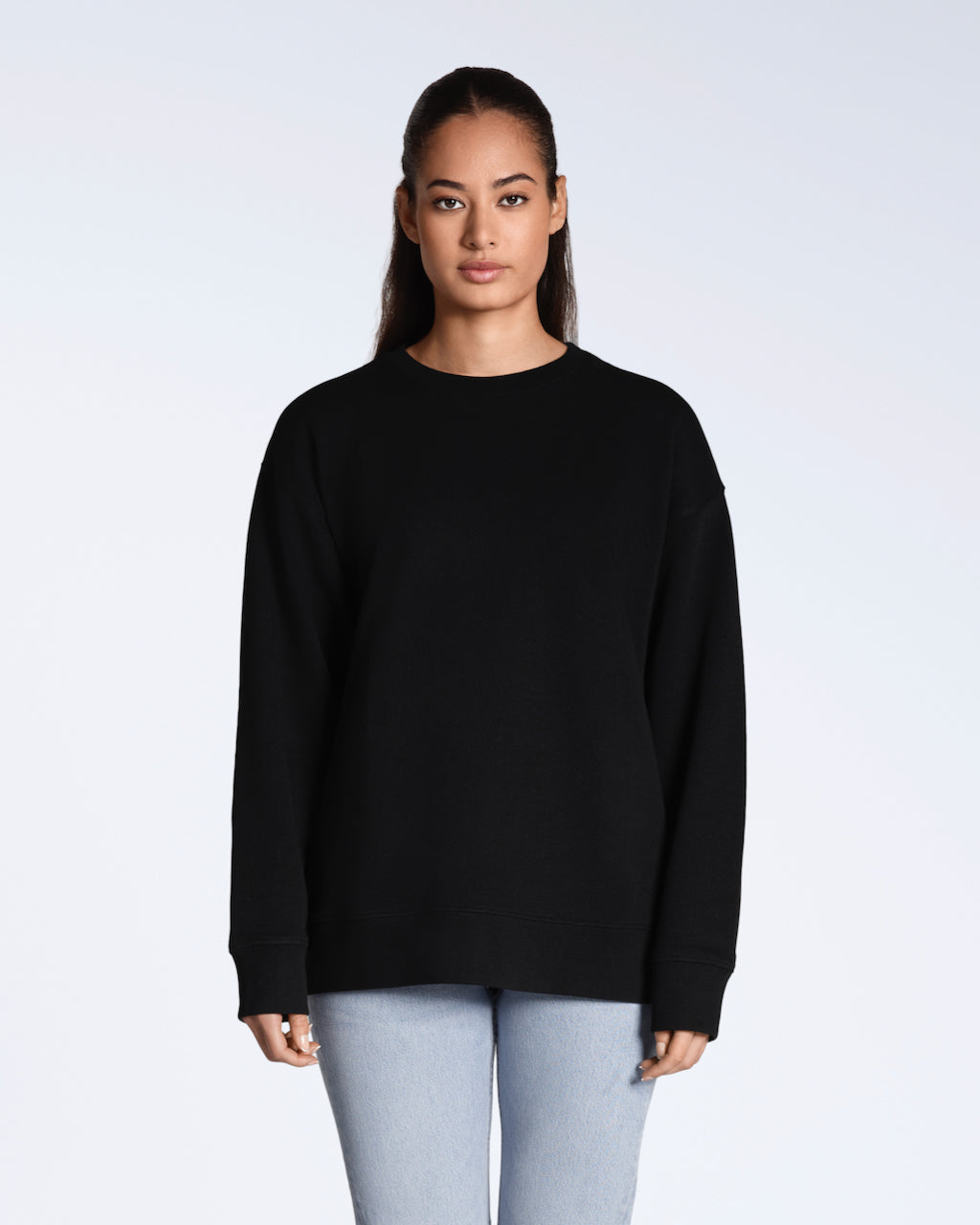 A woman facing front on, looking into the camera with her arms by her side, modelling a plain black, oversized, organic cotton sweatshirt.