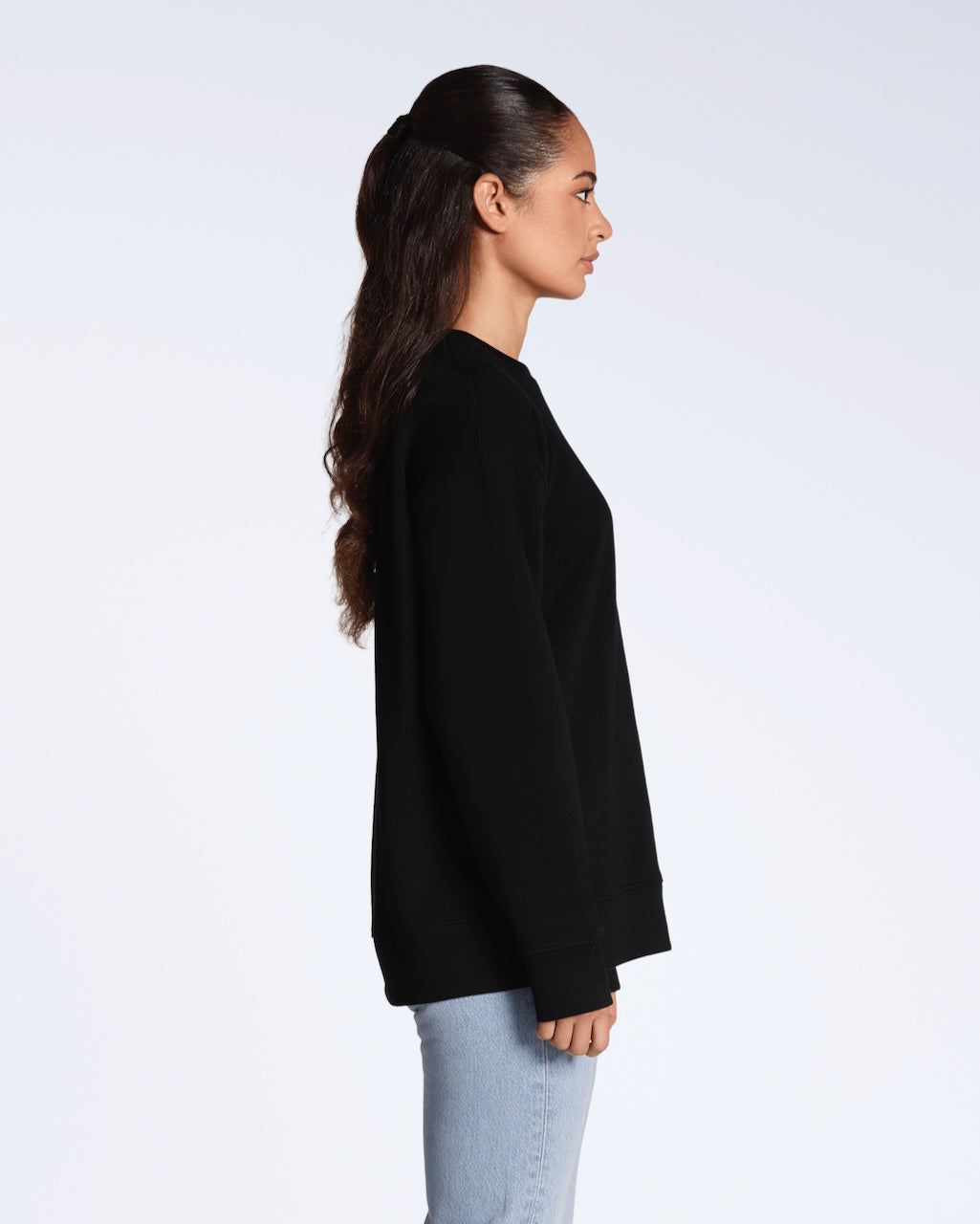 A woman facing side on, with her arms by her side, modelling a plain black, oversized, organic cotton sweatshirt.