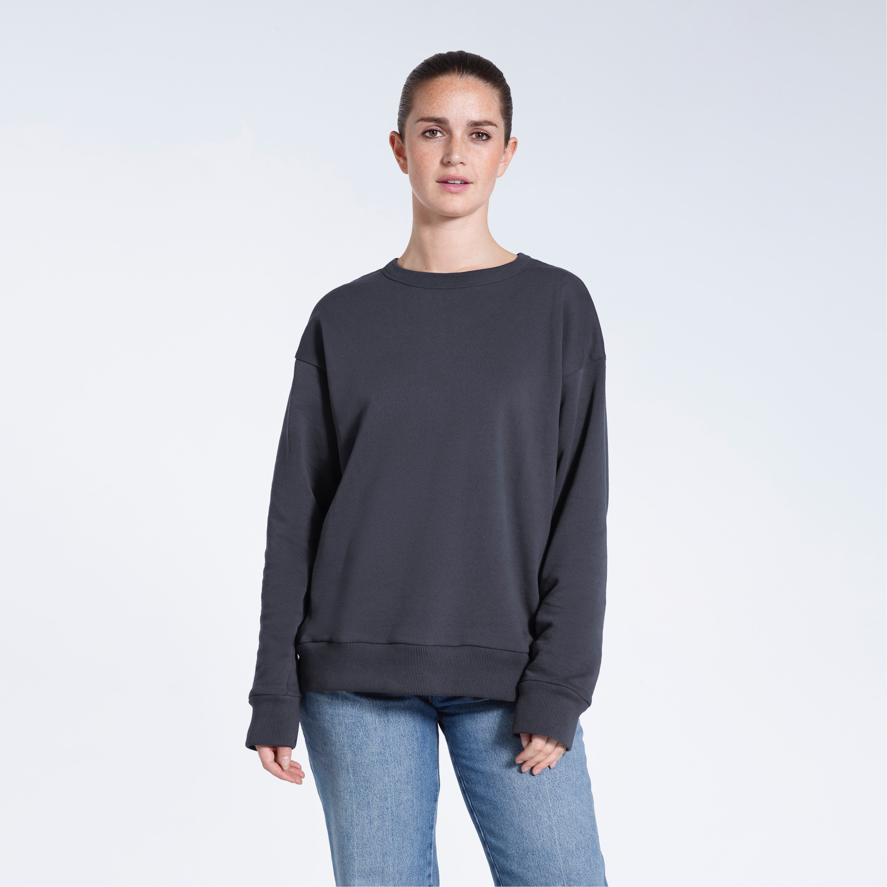A woman looking into the camera with her arms by her side, modelling a plain dark grey oversized organic cotton sweatshirt.