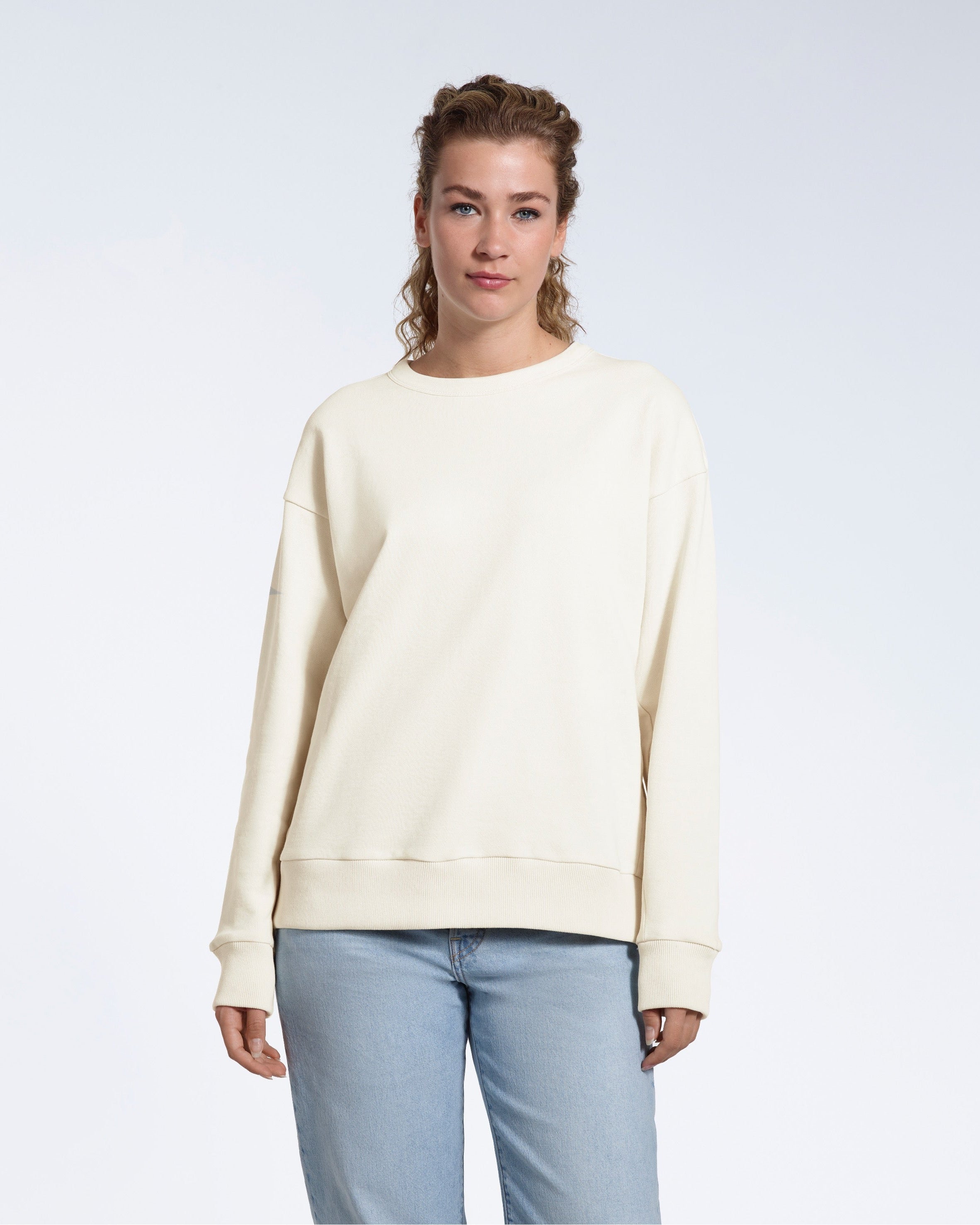 A woman looking into the camera with her arms by her side, modelling a plain ecru oversized organic cotton sweatshirt.