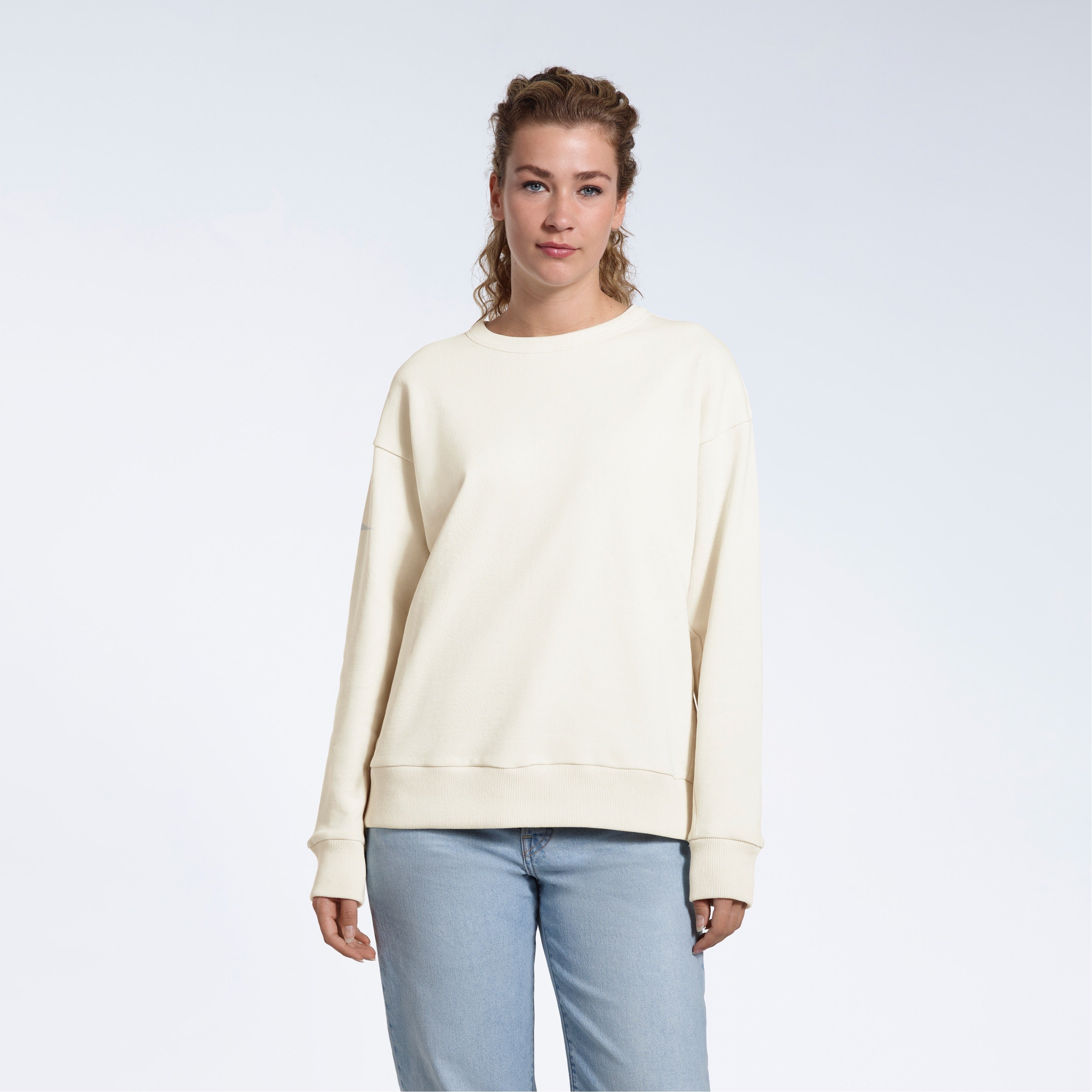 A woman looking into the camera with her arms by her side, modelling a plain ecru oversized organic cotton sweatshirt.