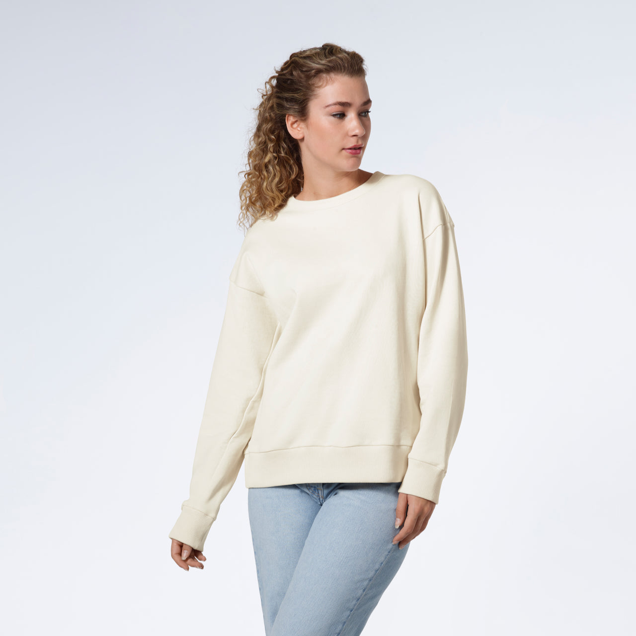 A woman looking away from the camera with her arms by her side, modelling a plain ecru oversized organic cotton sweatshirt.