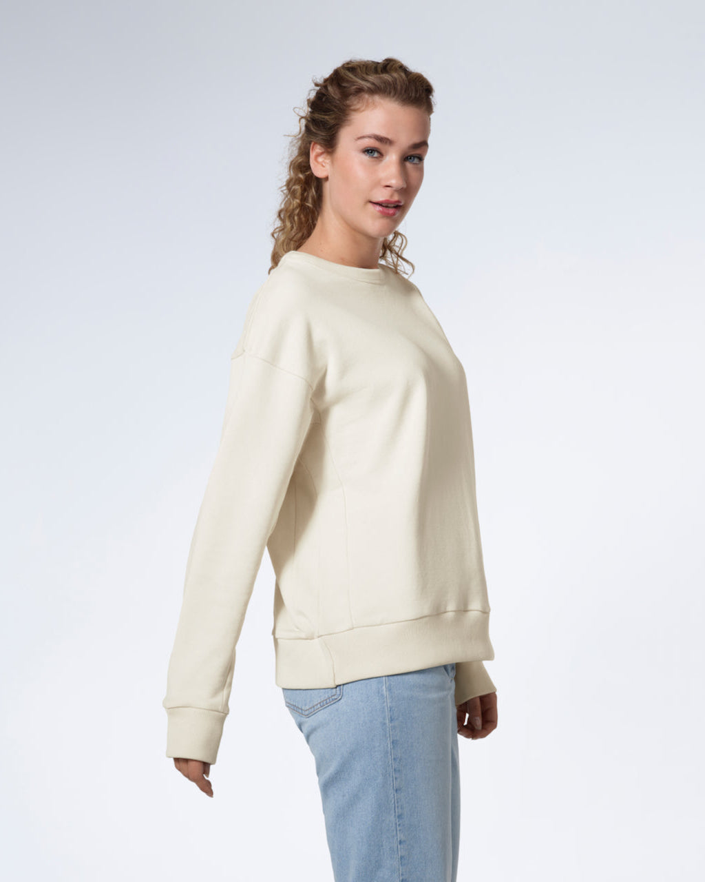 A woman facing side on looking into the camera, modelling a plain ecru oversized organic cotton sweatshirt.