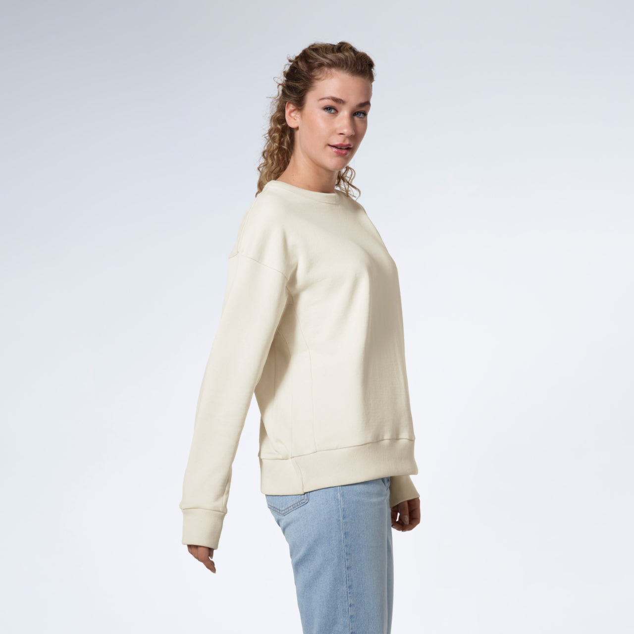 A woman facing side on looking into the camera, modelling a plain ecru oversized organic cotton sweatshirt.