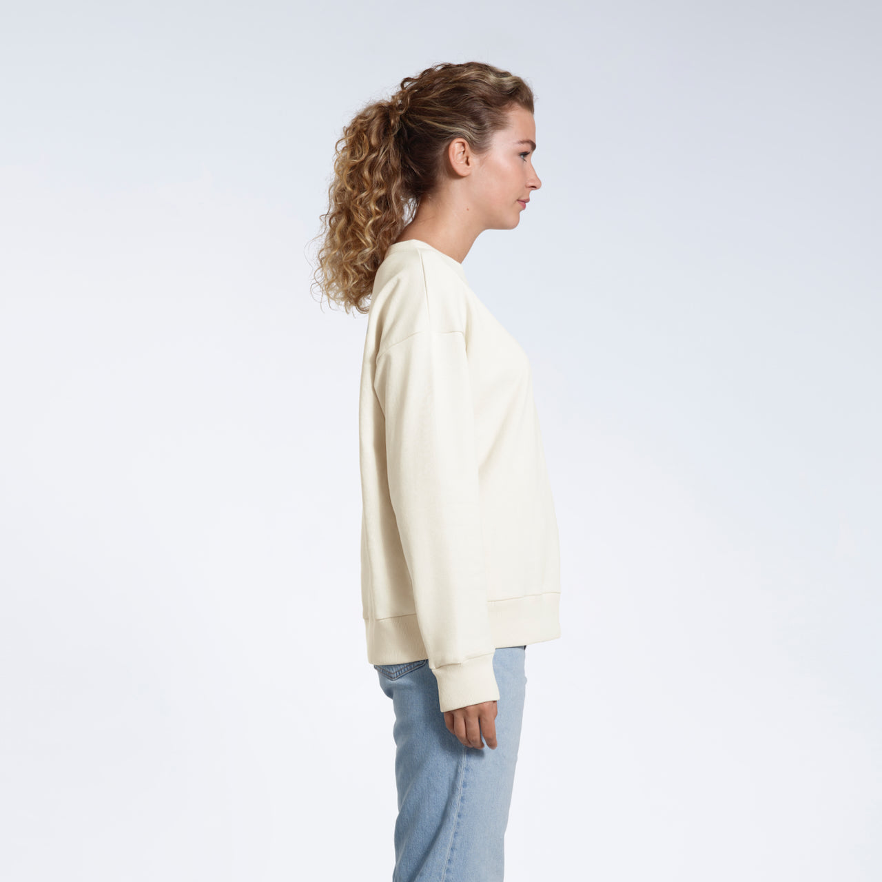 A woman facing side on with her arms by her side, modelling a plain ecru oversized organic cotton sweatshirt.
