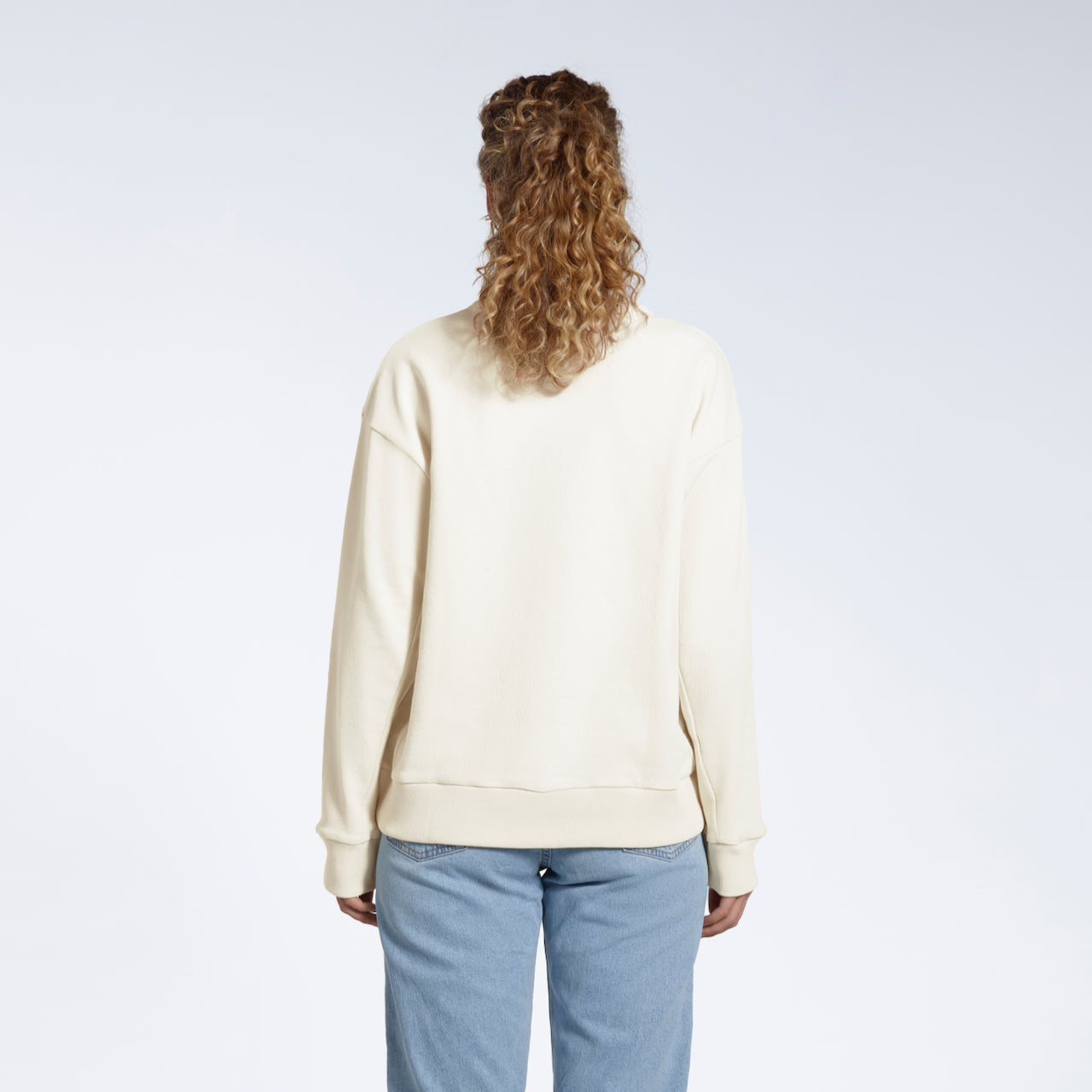 A woman facing away from the camera with her arms by her sides, modelling a plain ecru oversized organic cotton sweatshirt.
