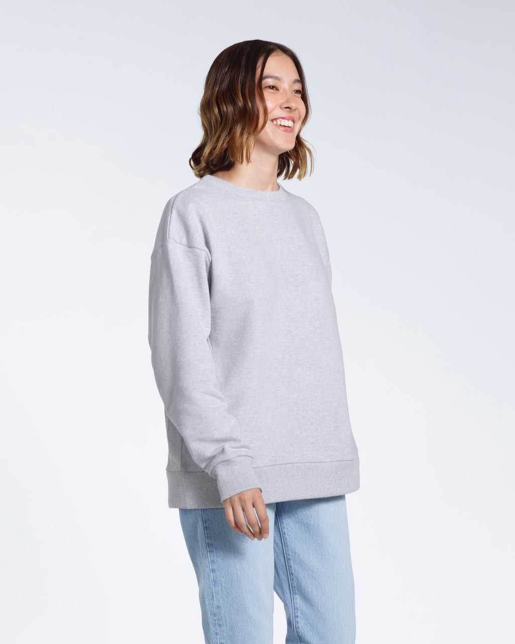 A woman smiling looking away from the camera, modelling a plain grey oversized organic cotton sweatshirt.