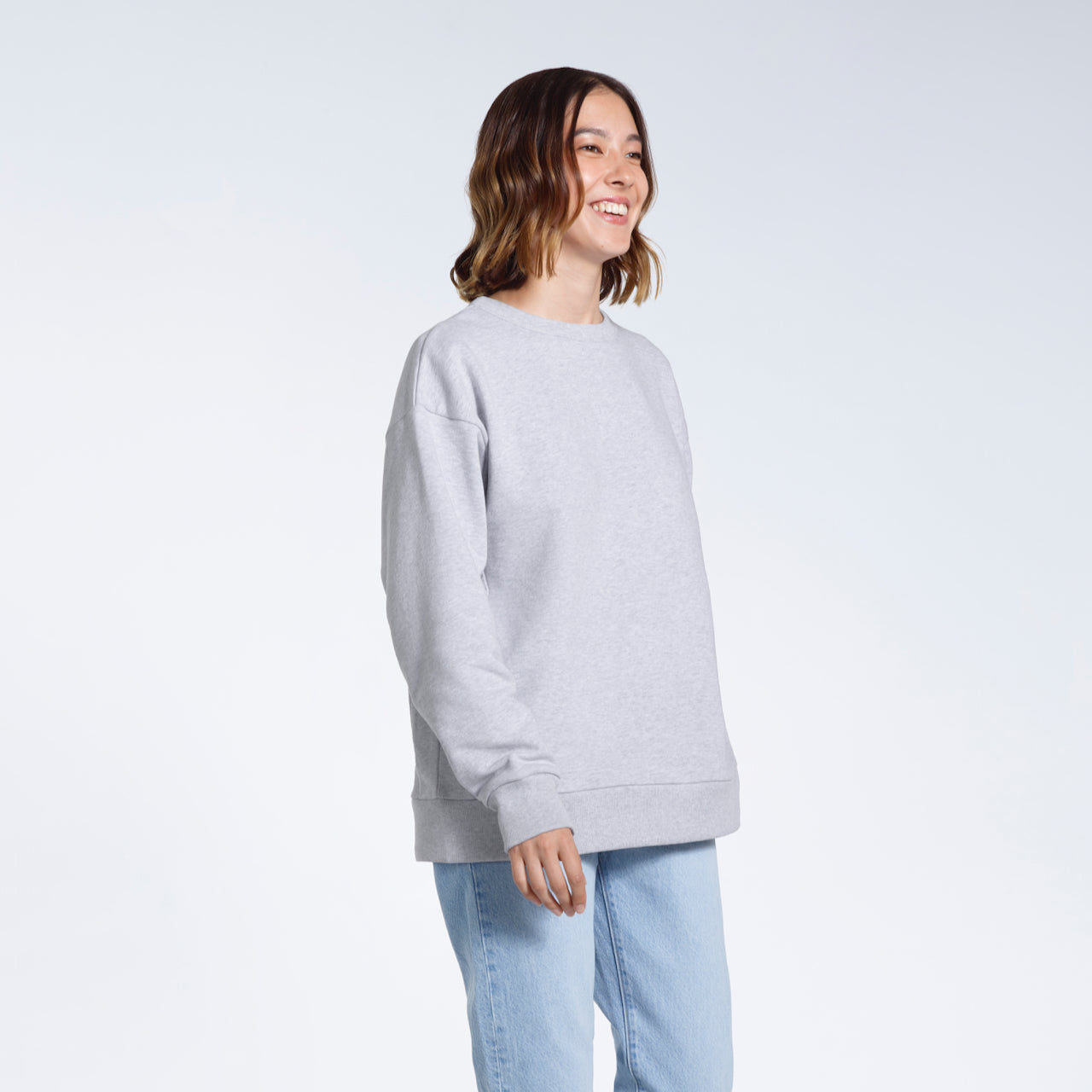 A woman smiling looking away from the camera, modelling a plain grey oversized organic cotton sweatshirt.