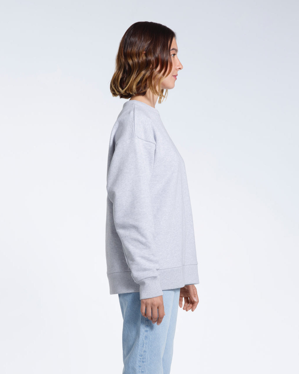 A woman facing side on with her arms by her side, modelling a plain grey oversized organic cotton sweatshirt.