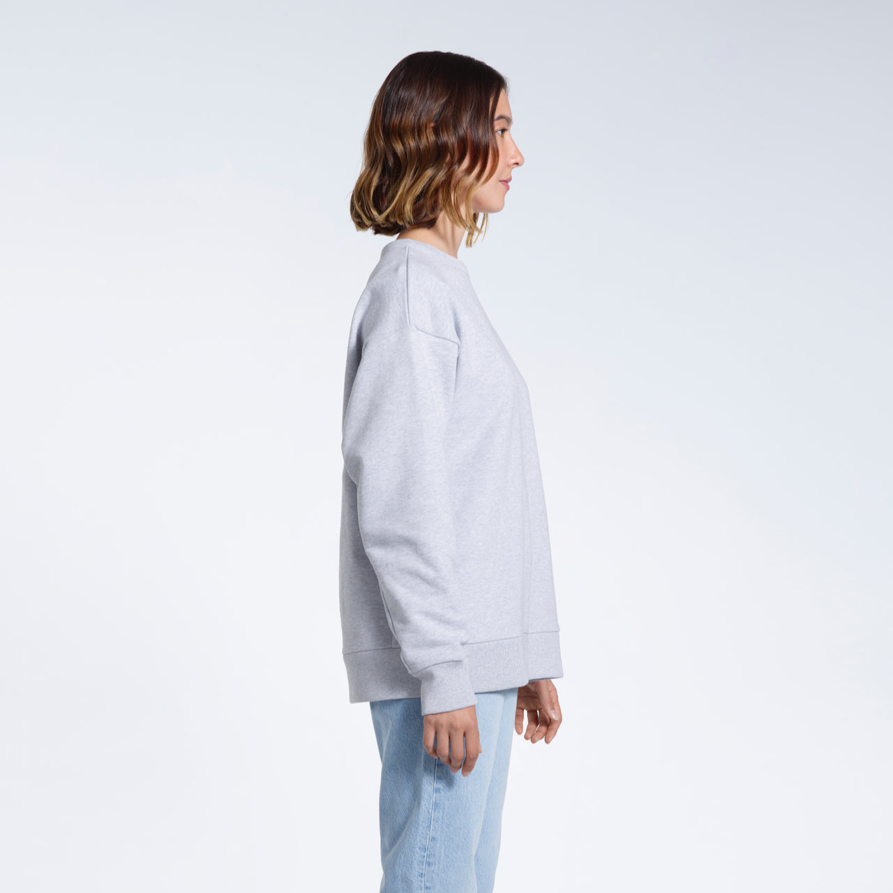 A woman facing side on with her arms by her side, modelling a plain grey oversized organic cotton sweatshirt.
