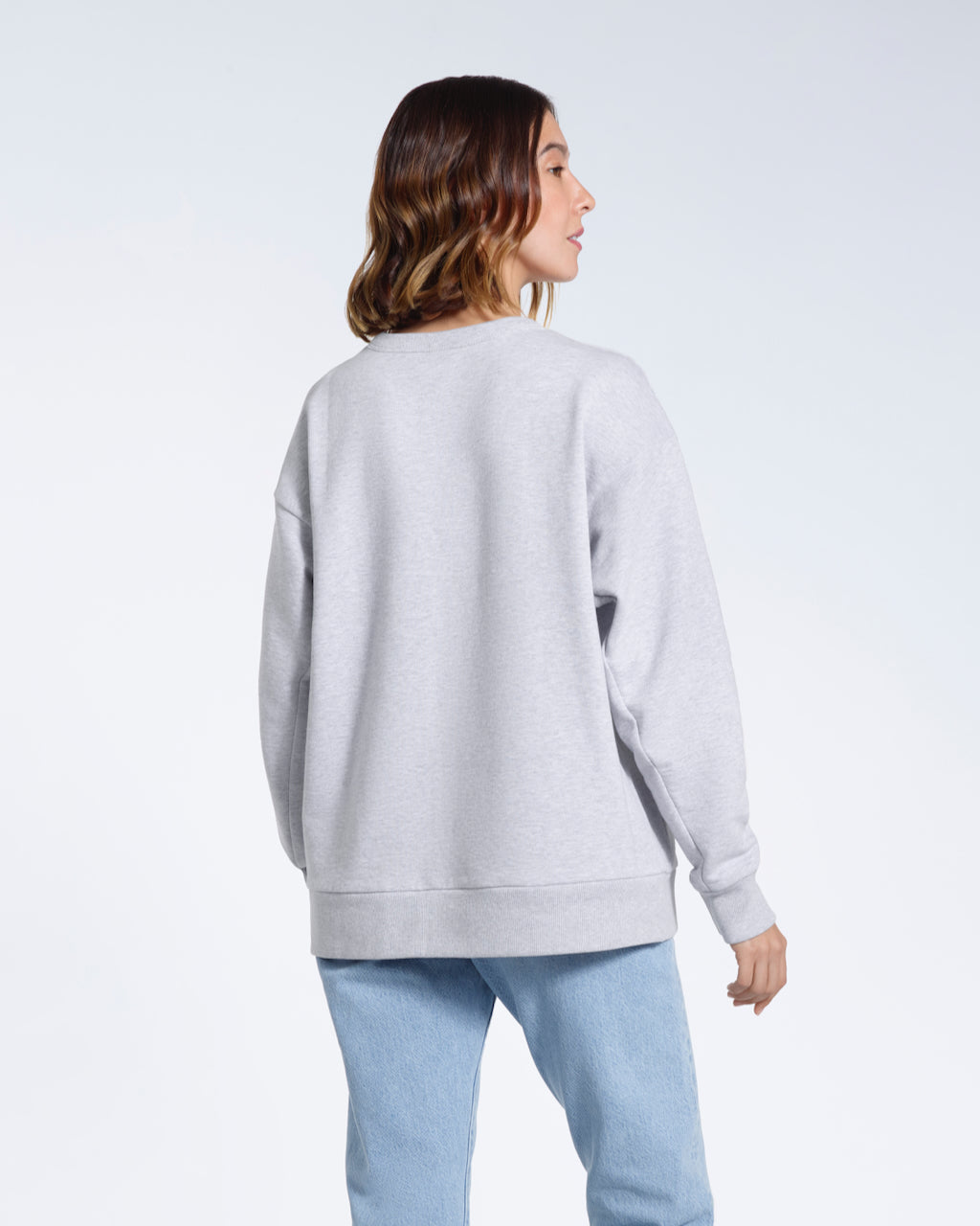 A woman facing away from the camera with her arms by her sides, modelling a plain grey oversized organic cotton sweatshirt.