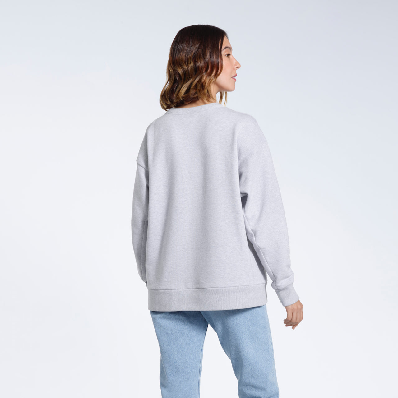 A woman facing away from the camera with her arms by her sides, modelling a plain grey oversized organic cotton sweatshirt.